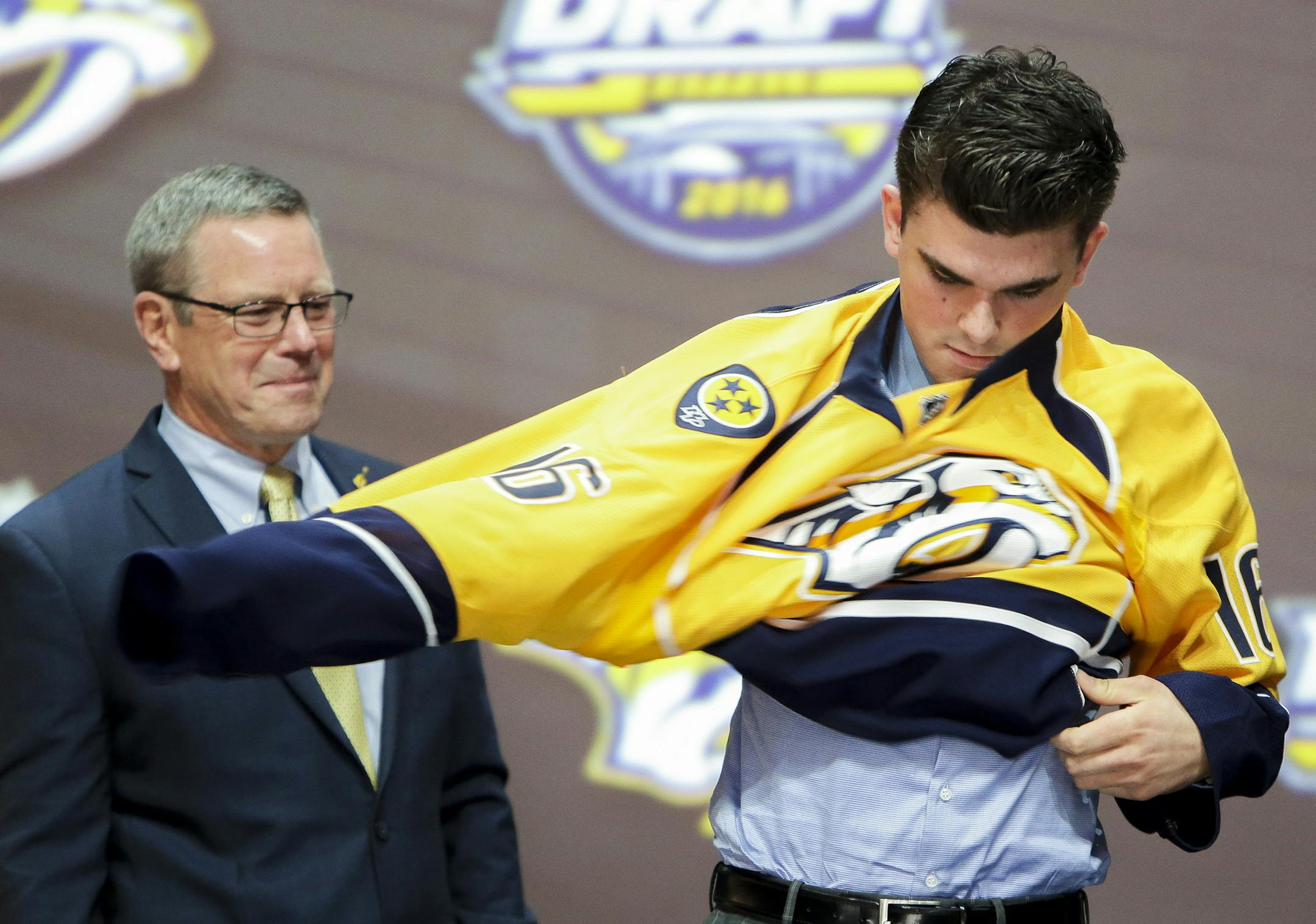 June 24, 2016: Dante Fabbro dons the Predators jersey after he was selected as the 17th pick in the first round of the 2016 NHL Entry Draft at First Niagara Center in Buffalo, NY. at left is Predators assistant general manager Paul Fenton. (Photo by John Crouch/Icon Sportswire.) (Icon Sportswire via AP Images) ORG XMIT: 263699