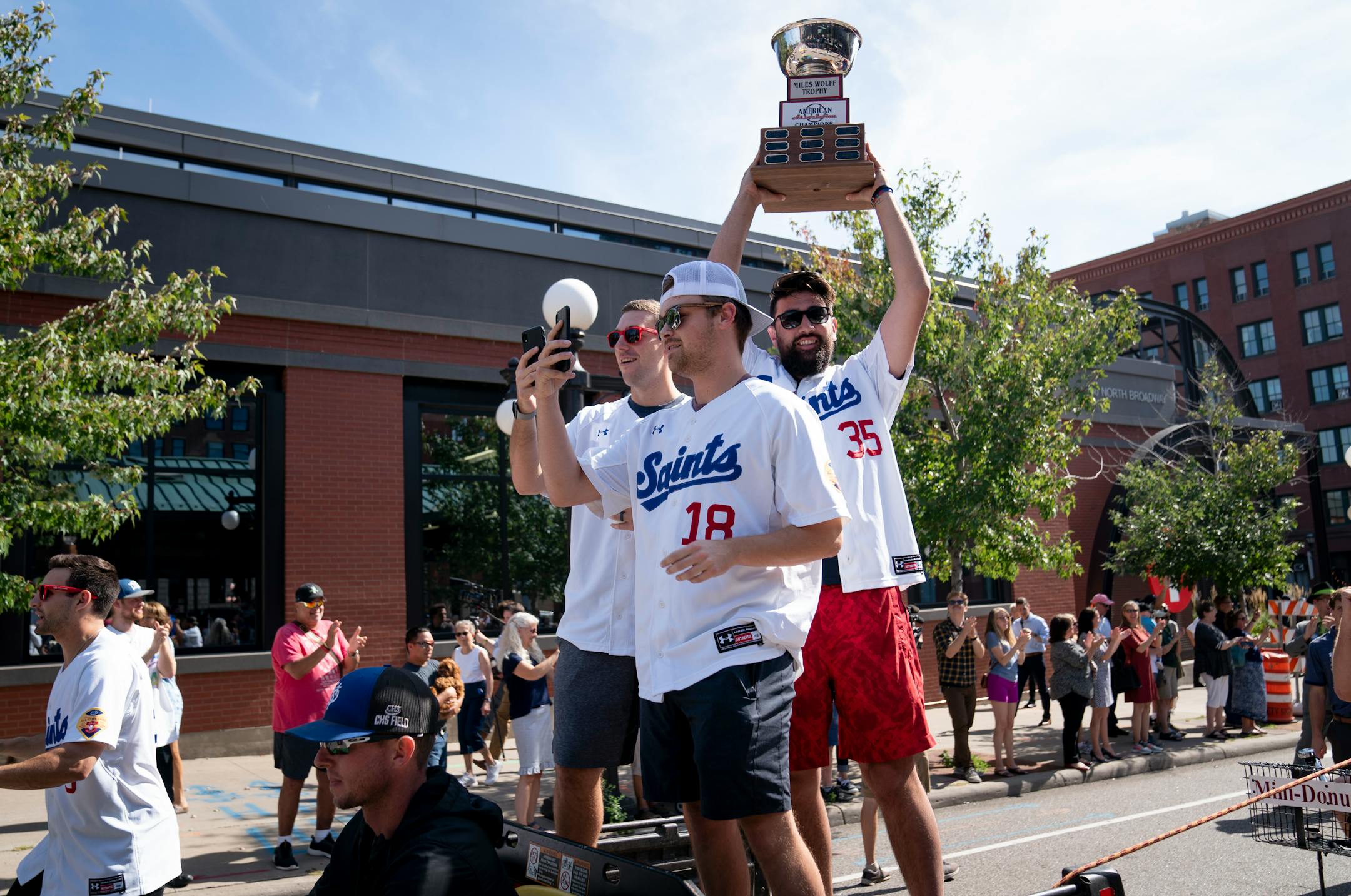 Saints player Todd Van Steensel held up the American Association championship trophy while standing on the back of a moving vehicle during the Saints' one-block victory parade in St. Paul on Monday.