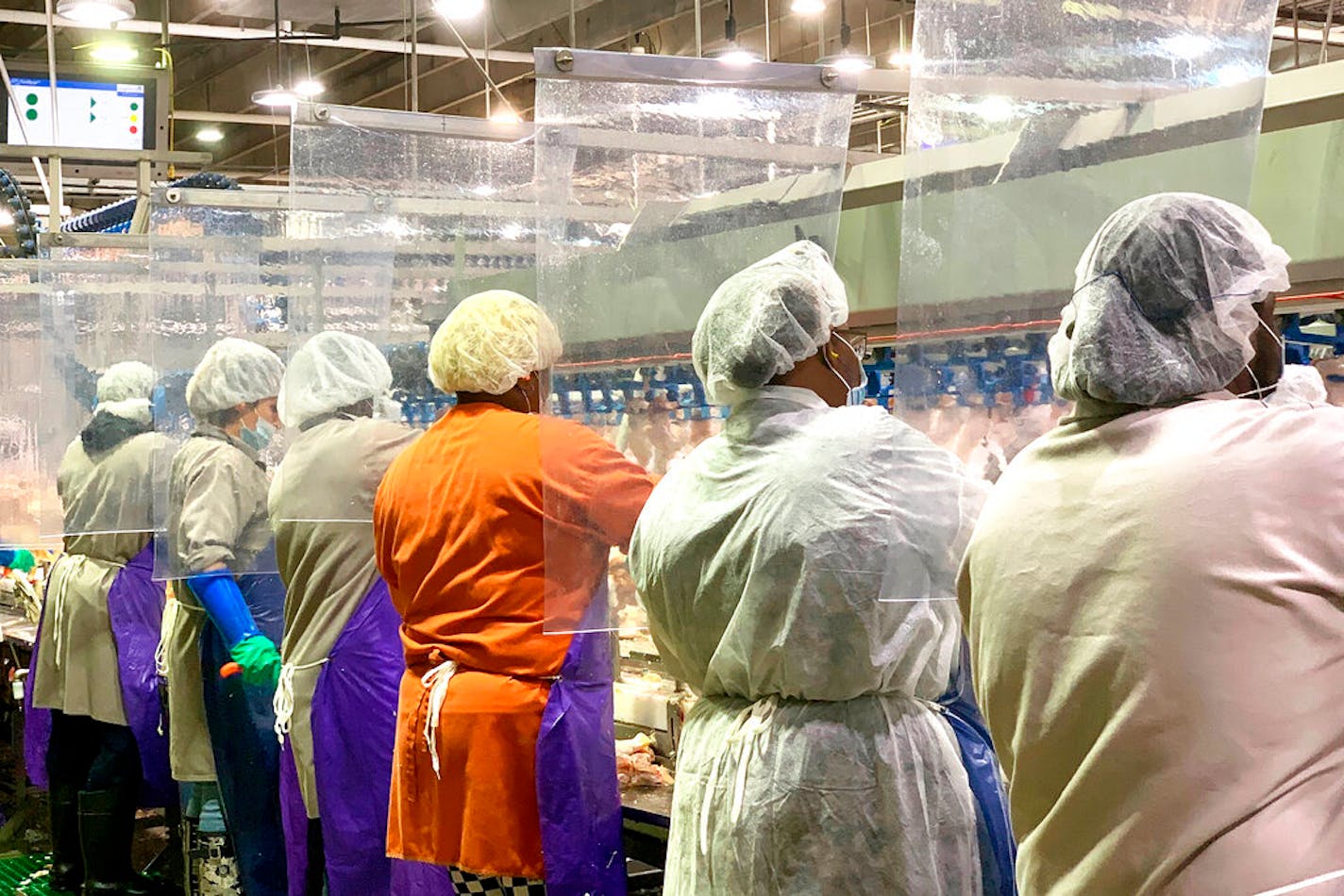 Tyson Foods workers wear protective masks and stand between plastic dividers at a poultry processing plant in Camilla, Ga. Tyson has added the plastic dividers to create separation between workers because of the coronavirus outbreak.