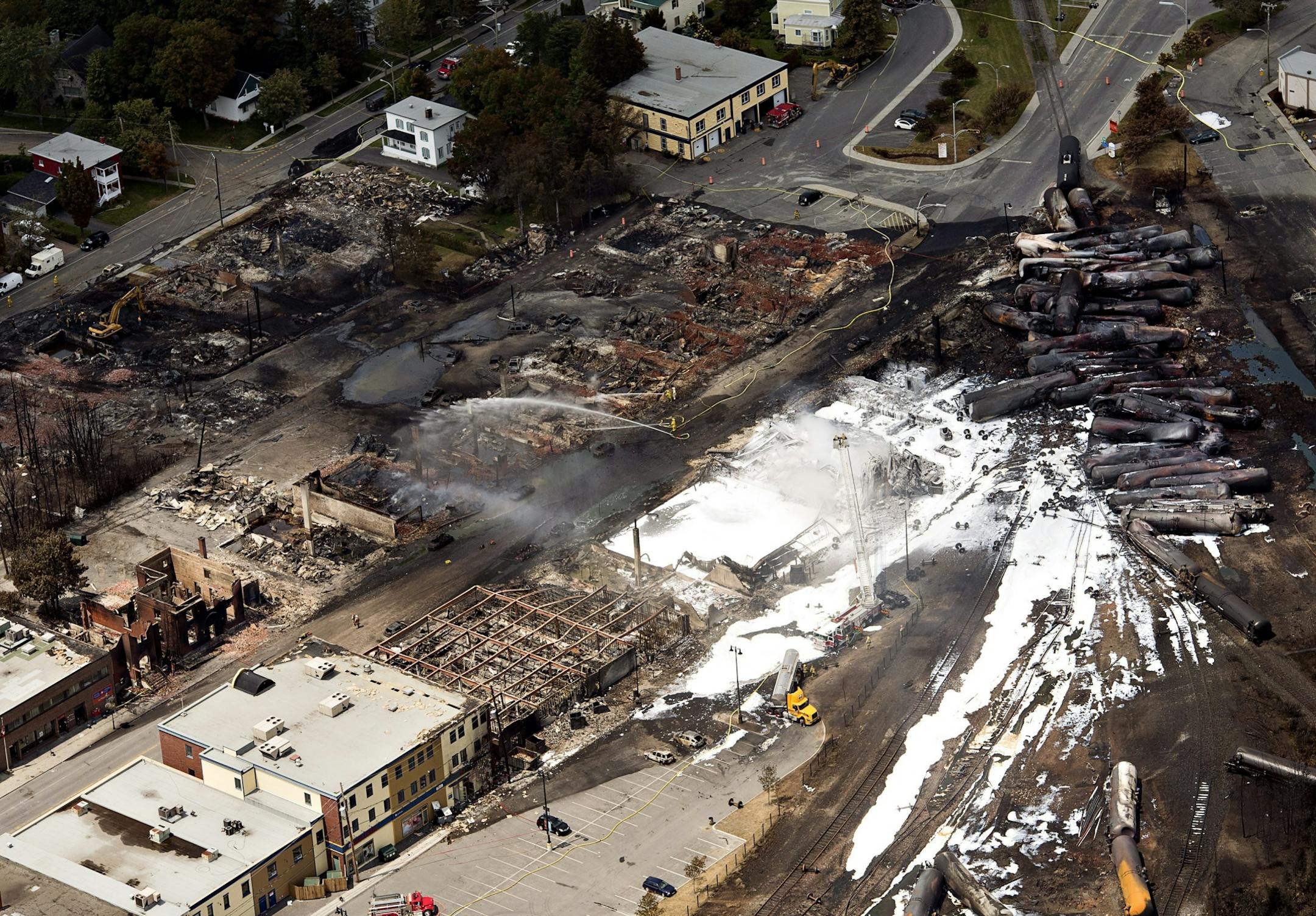 The downtown core lays in ruins as fire fighters continue to water smoldering rubble Sunday, July 7, 2013 in Lac Megantic, Quebec. A runaway train derailed Saturday igniting tanker cars carrying crude oil.