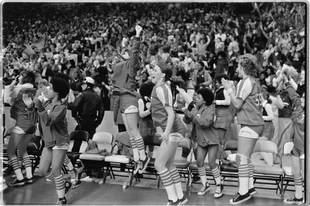 St. Paul Central players celebrated their victory in the first official Girls' State Basketball Tournament Class AA semifinal game in 1976. Players include, from left to right, Georgetta Hawkins (#3, with jacket), Teresa Tierney (jumping with fists clenched), Bonnie Lubben (arms down), Kim Miller (with jacket, clapping at bench) and Debbie Krengel (#55).