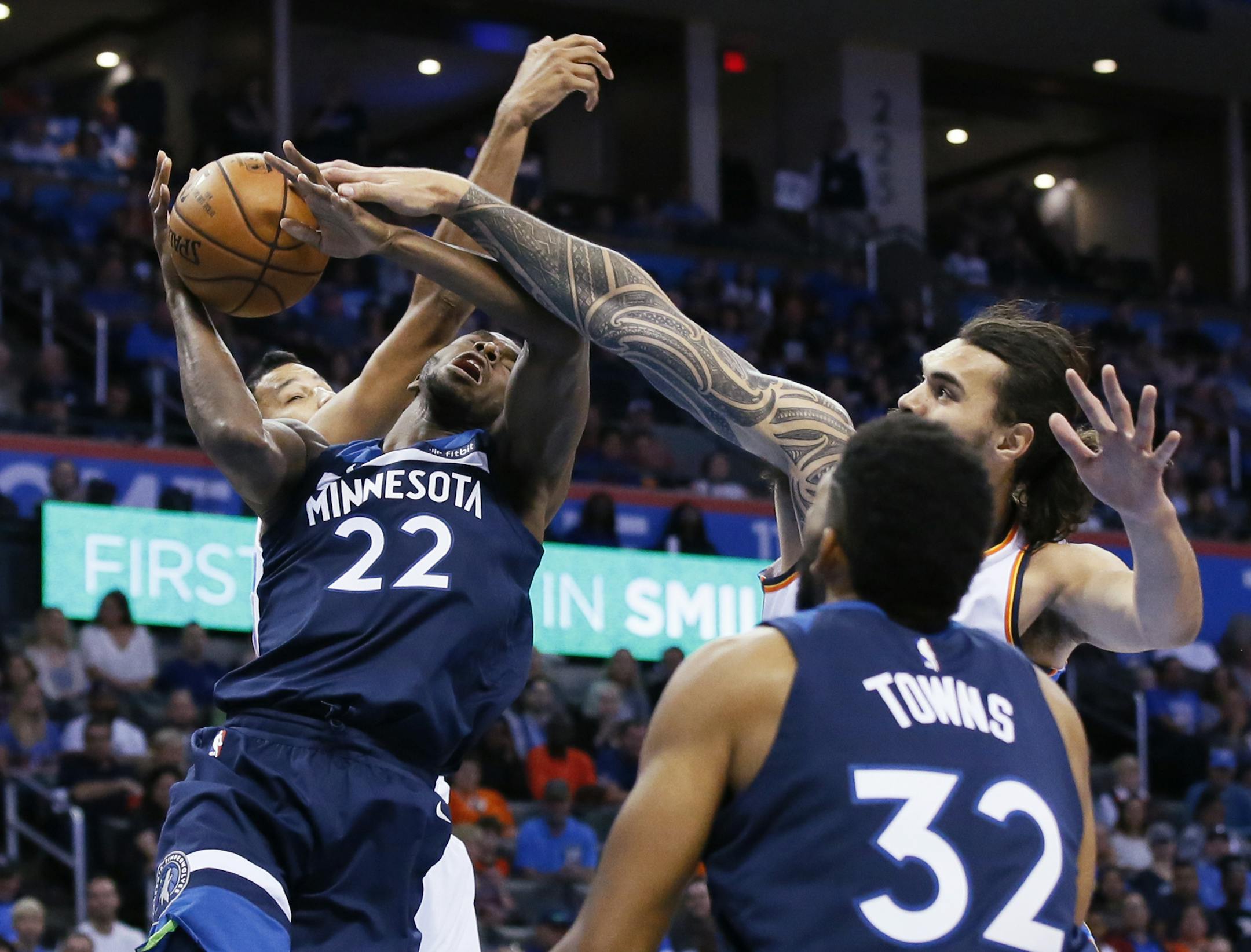 Minnesota Timberwolves guard Andrew Wiggins (22) is fouled by Oklahoma City Thunder center Steven Adams, right, as he shoots between Adams and Andre Roberson, left, in the first quarter of an NBA basketball game in Oklahoma City, Sunday, Oct. 22, 2017. (AP Photo/Sue Ogrocki)