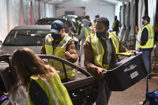 Carlos Remigio, right, a volunteer, and Michael Lindsay, left of center, a Ramsey County employee, worked to unload the car of an election judge, collecting sealed ballot boxes and voting equipment.