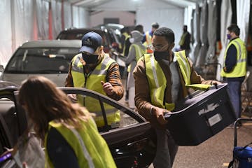 Carlos Remigio, right, a volunteer, and Michael Lindsay, left of center, a Ramsey County employee, worked to unload the car of an election judge, coll