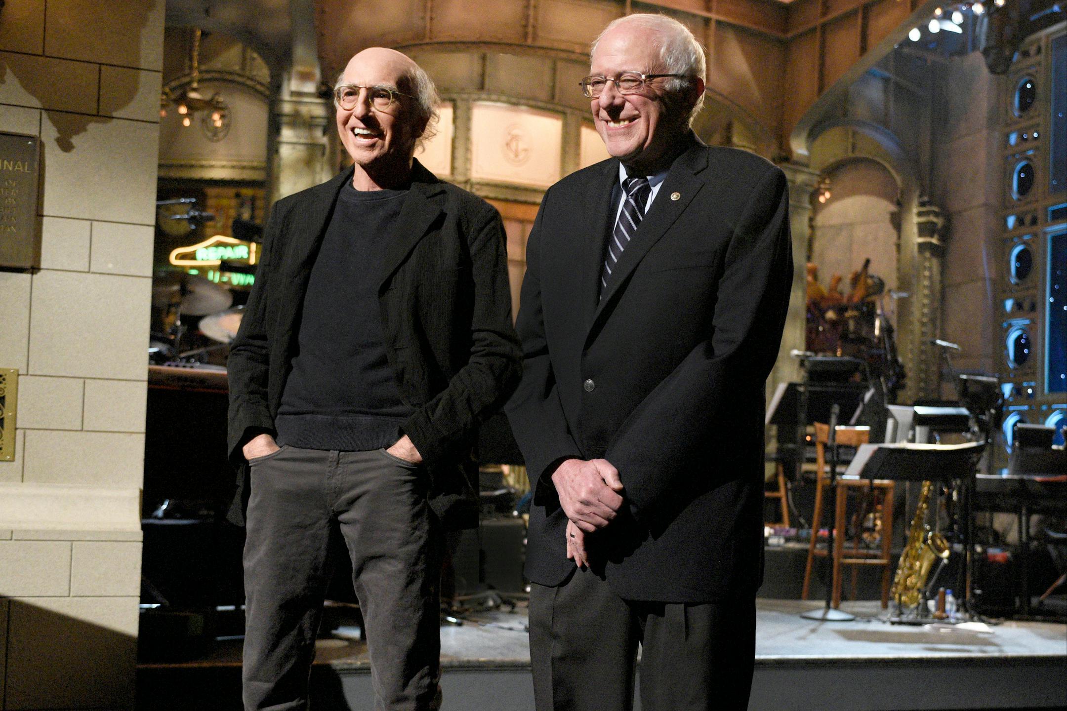 This Saturday, Feb. 6, 2016 photo provided by NBC shows, Larry David, left, and Democratic presidential candidate Sen. Bernie Sanders, introducing musical guest The 1975 on the "Larry David" episode of "Saturday Night Live," in New York. Sanders made a cameo appearance on "Saturday Night Live" three days before the New Hampshire primary, appearing in a skit with host David, the comic who has done a dead-on impersonation of him. Sanders is the third presidential candidate to appear on "SNL" this