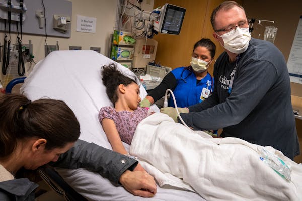 Registered nurse Joe Schwartz, from right, finds a vein to start an IV with the help of RN Shanna Jorgenson for patient Juliana Jones, 10, as her moth