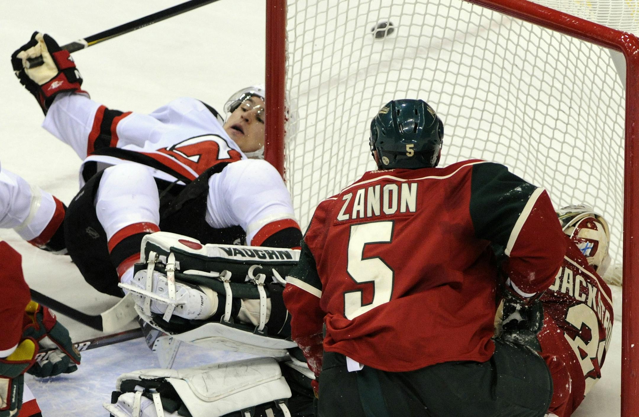 New Jersey Devils' Zach Parise, left, trips over Minnesota Wild goalie Niklas Backstrom, of Finland, lower right, after attempting a shot in the first period of an NHL hockey game, Friday, Dec. 2, 2011, in St. Paul, Minn.