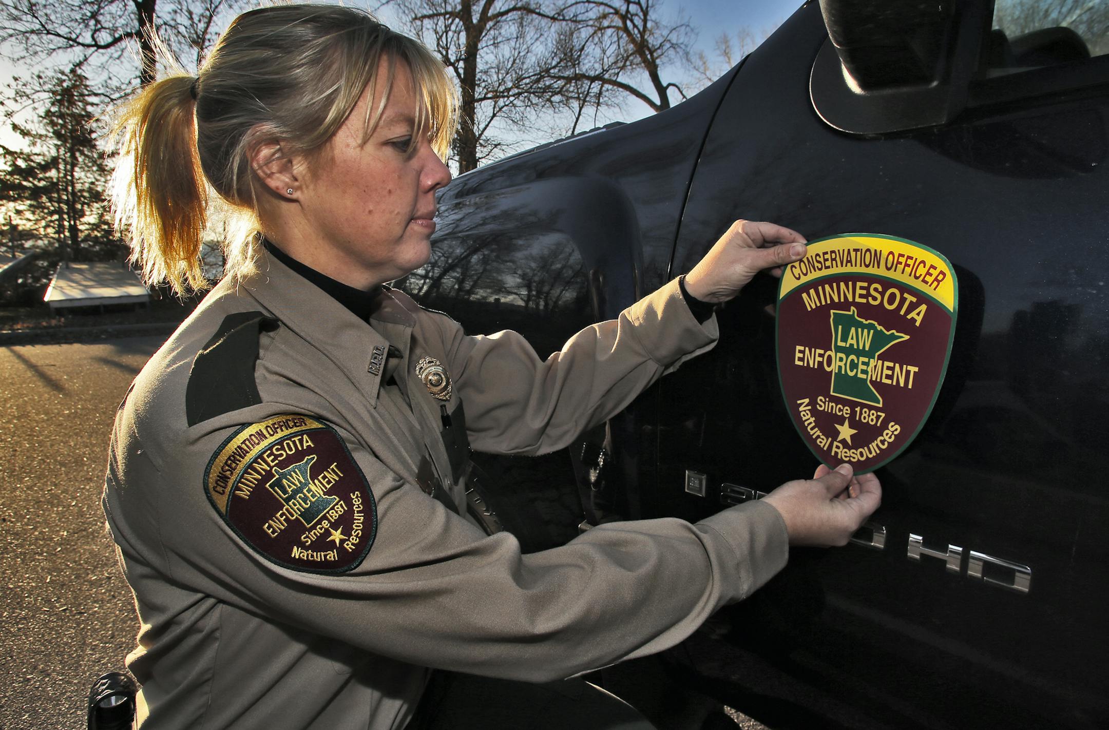 Jackie Glaser is a Minnesota DNR officer working on the west side of the Twin Cities. Glaser juggles her work duties with the responsibilities of being a mother of three young sons. Photos taken on the shore of Lake Waconia. Jackie Glaser places a magnetic DNR shield on the door of DNR vehicle. (MARLIN LEVISON/STARTRIBUNE(mlevison@startribune.com)