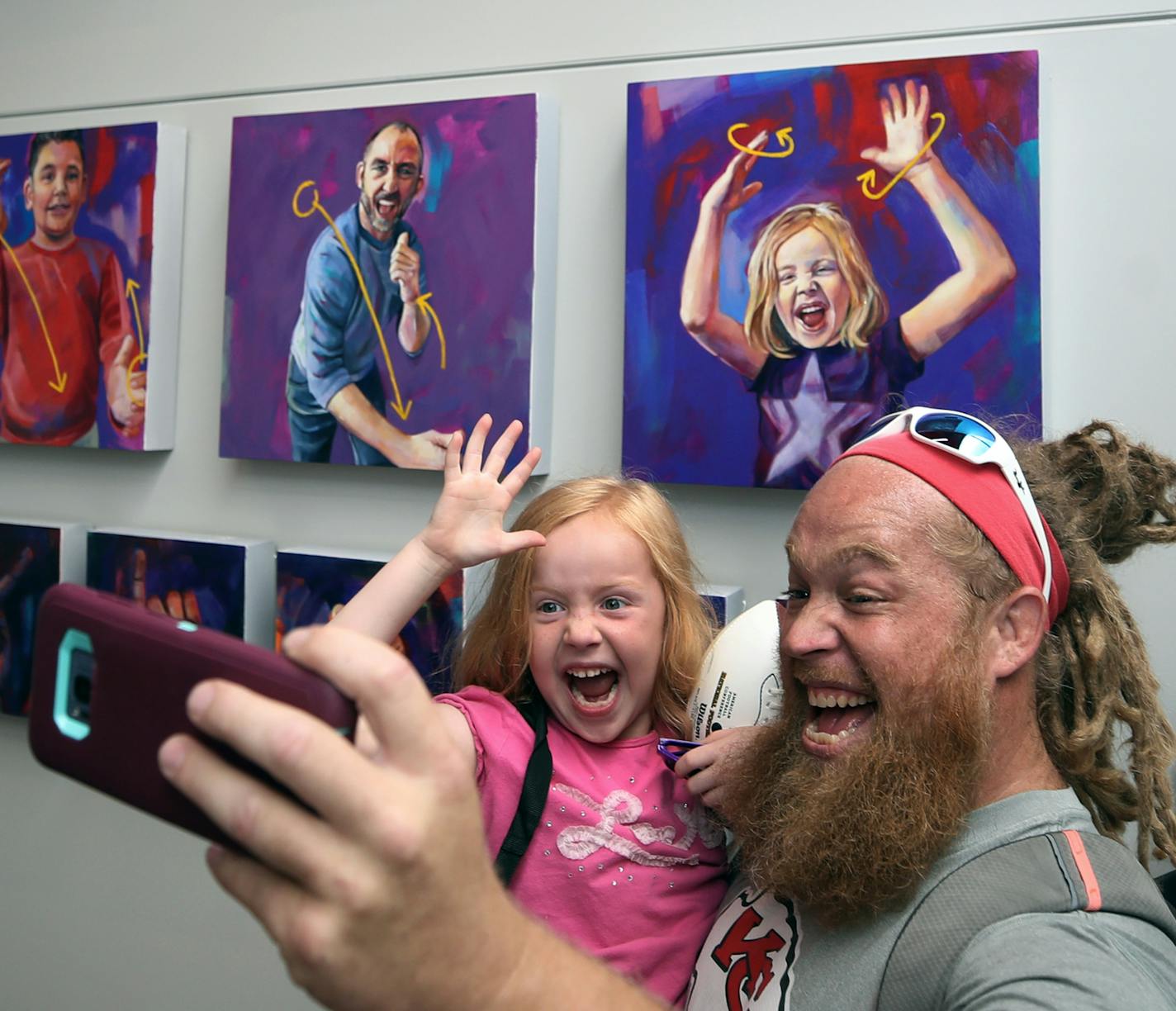 Teddie Barnett took a photo with is daughter Lana Barnett 6; Lana is a student at the Metro Deaf School. Students from the school posed for pictures as they used American Sign Language to communicate. Artist Leslie Barlow painted the outline of each photo and added a light purple background, but left the majority of the painting available for Metro Deaf Students to fill in using a paint-by-the numbers system. The students got to see the work at the Minnesota Vikings training camp at TCO Performa