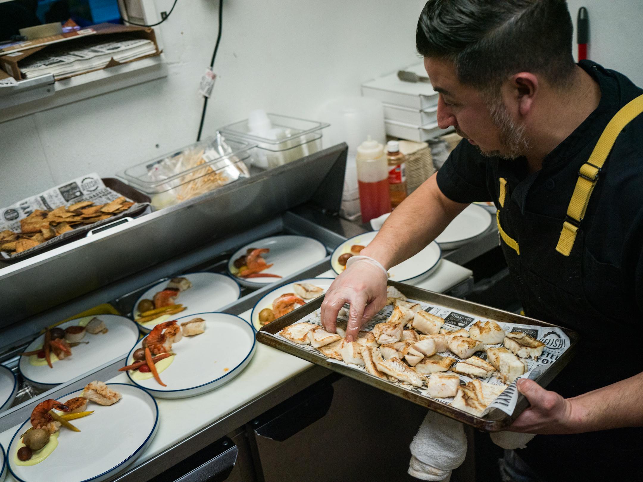 Chef Cristian de Leon plates up a seafood dish in the crowded kitchen.