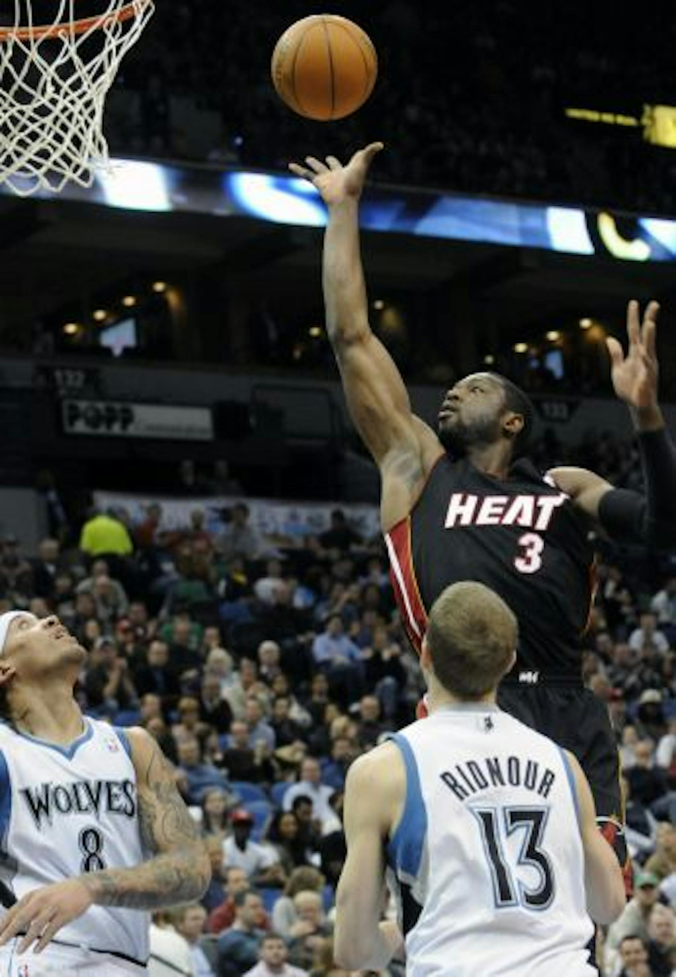 Minnesota Timberwolves' Michael Beasley, left, and Luke Ridnour, right, look on as Miami Heat's Dwyane Wade shoots during the first half of an NBA basketball game Friday, April 1, 2011 in Minneapolis.