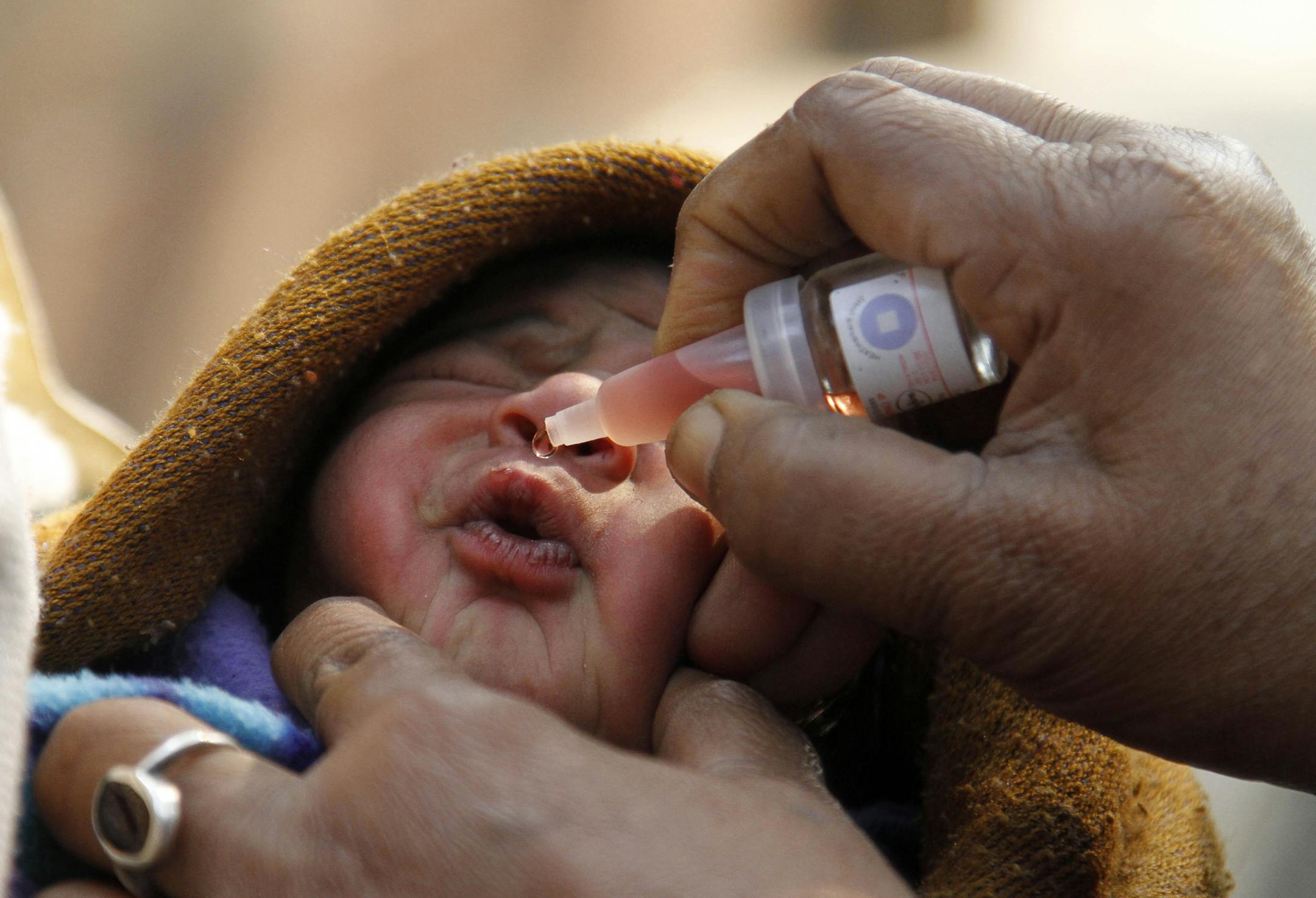 A health worker administers pulse polio drop to a newborn baby in India.