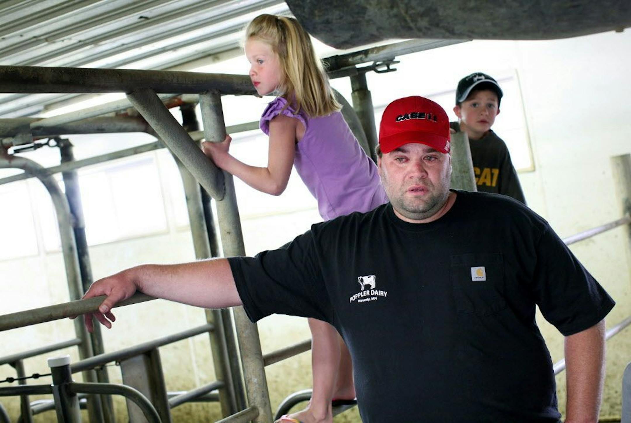 While his children Dani, 7, left, and Shayne, 5, play in the milking parlor, dairy farmer Harlan Poppler gets emotional as he considers the many dead cows he had to carry out of his barns over recent years at Poppler Dairy Farm in Waverly July 25, 2013. His cows were affected by stray currents from a local electric company.