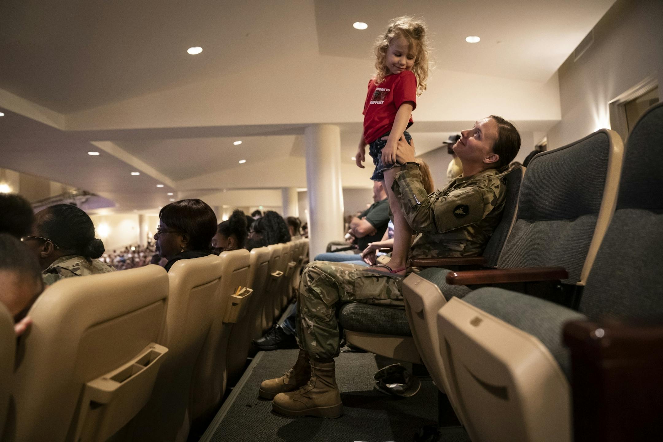 Ally Chafee looked back as her mom Jeanette Chafee as she stood on her lap to get a better view during the family deployment ceremony in Eden Prairie, Minn., on Friday, September 20, 2019.