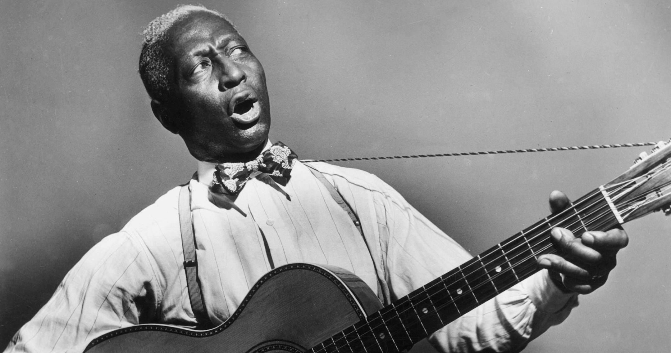 circa 1935: Promotional portrait of American blues musician Huddie 'Lead Belly' Ledbetter (1889 - 1949) playing a 12-string guitar and singing. (Photo by Hulton Archive/Getty Images)