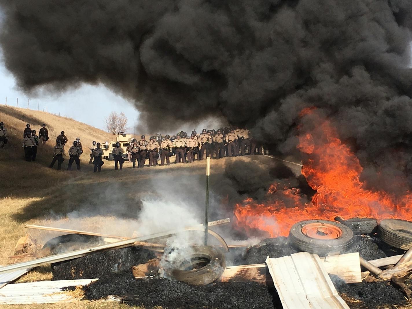 Tires burn as armed soldiers and law enforcement officers stand in formation on Thursday, Oct. 27, 2016, to force Dakota Access pipeline protesters off private land where they had camped to block construction.