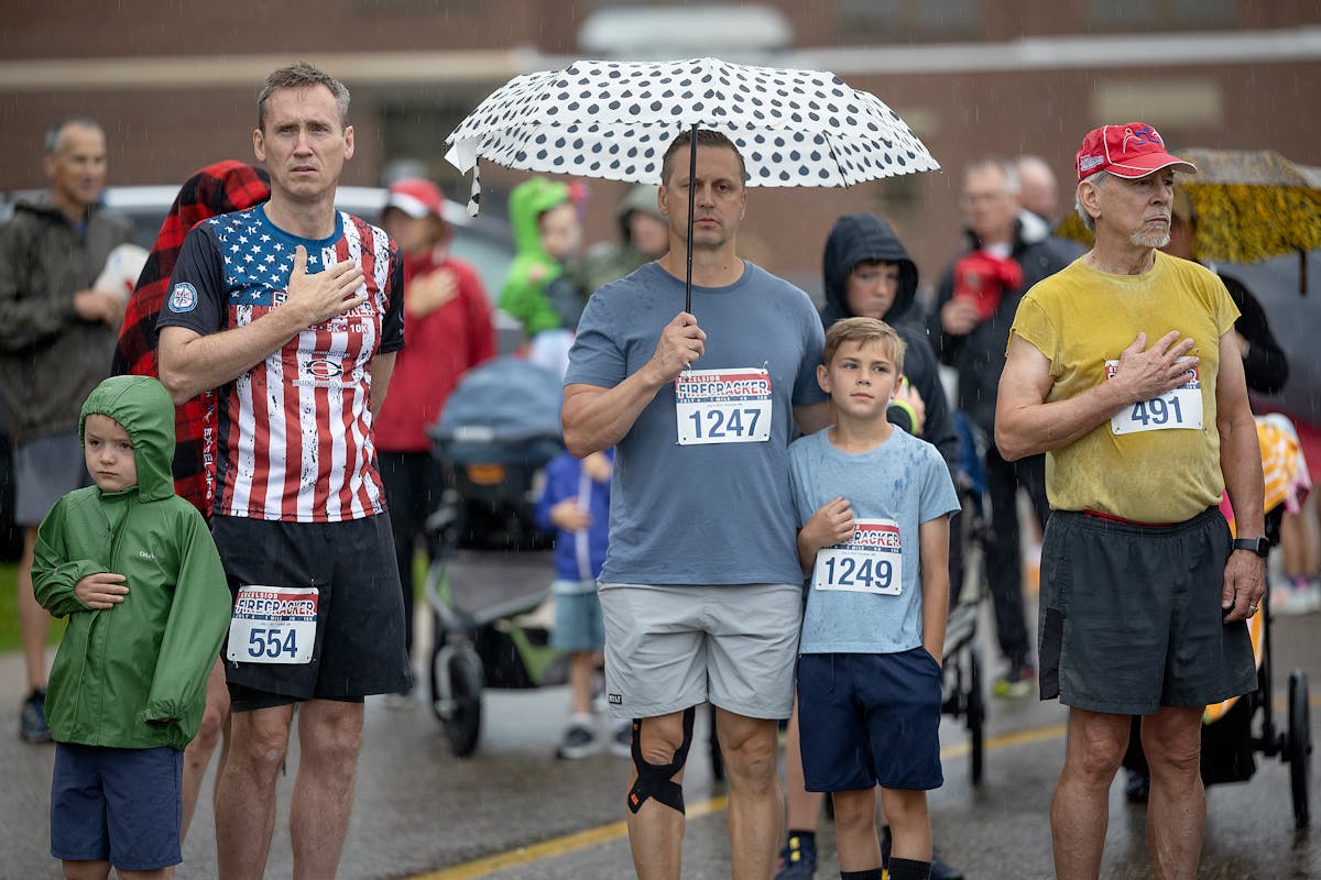 Runners stand for the National Anthem before the one-mile race at the Excelsior Firecracker Run on Thursday.