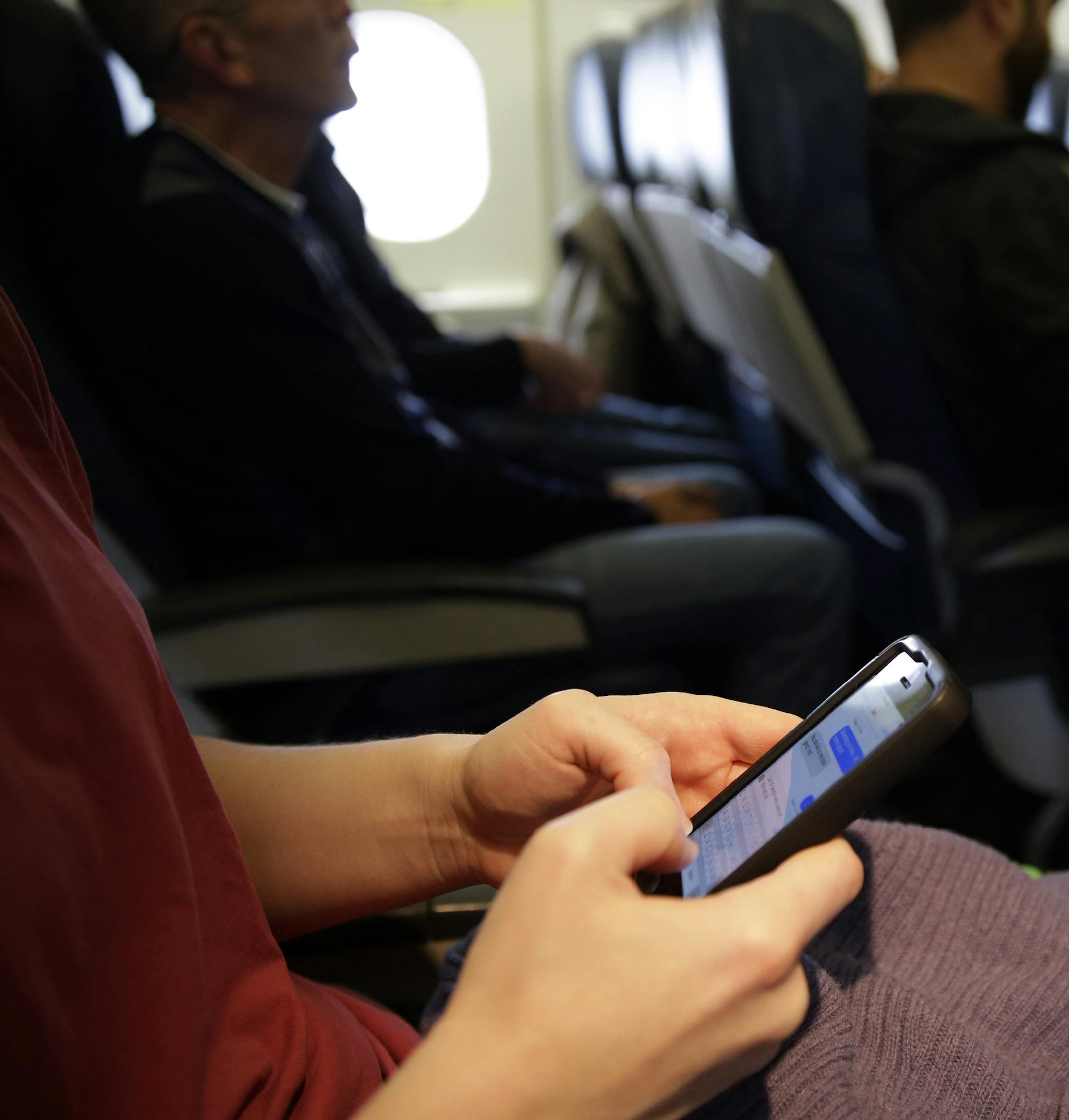 FILE - In this Oct. 31, 2013, file photo, a passenger checks her cell phone before a flight in Boston. The Federal Communications Commission might be ready to permit cellphone calls in flight. Old concerns about electronics being a danger to airplane navigation have been debunked. And carriers could make some extra cash charging passengers to call a loved one from 35,000 feet. But that extra money might not be worth the backlash from fliers who view overly-chatty neighbors as another inconvenien