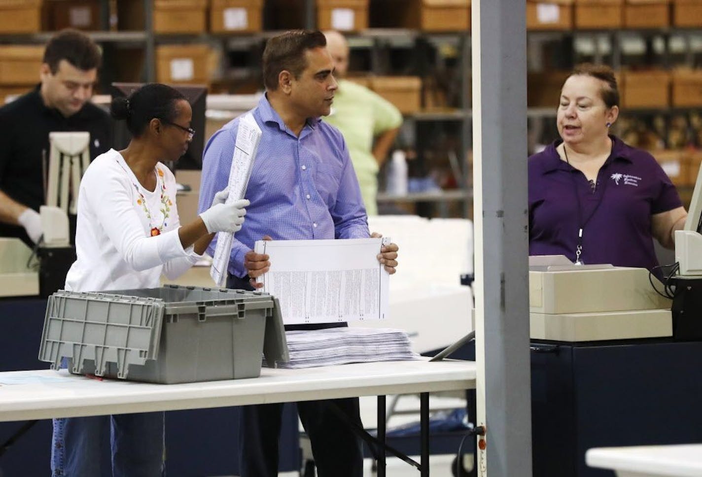 Employees at the Palm Beach County Supervisor of Elections office feed ballots through a machine as they count votes during a recount, Tuesday, Nov. 13, 2018, in West Palm Beach, Fla.