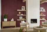 Living room with deep ruby red accent wall at back, boxy white fireplace to ceiling with shelving and art objects, chairs around coffee table and cabinet at back left with plant and vases.