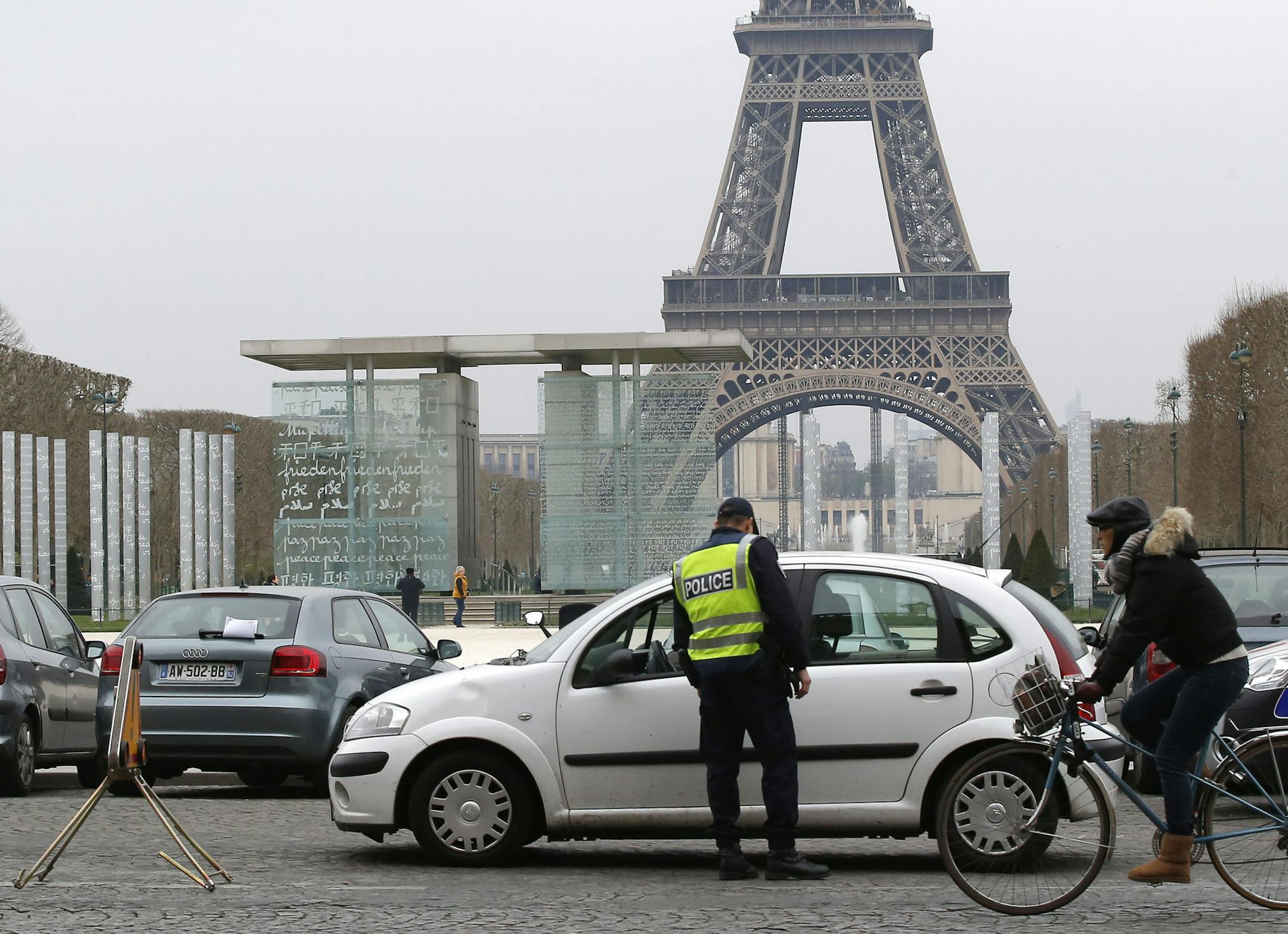 A police officer controls vehicle near the Eiffel Tower as a bicycle passes by in Paris, Monday, March 17, 2014. Cars with even-numbered license plates are prohibited from driving in Paris and its suburbs Monday, following a government decision over the weekend. Paris is taking drastic measures to combat its worst air pollution in years, banning around half of the city's cars and trucks from its streets in an attempt to reduce the toxic smog that's shrouded the City of Light for more than a week