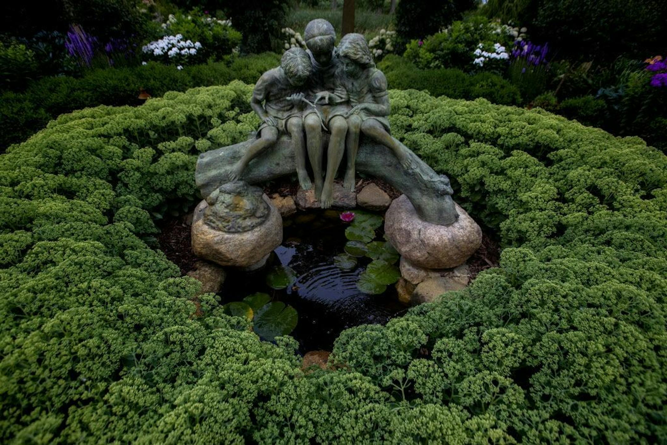 A bronze sculpture is perched over a goldfish pond framed by Autumn Fire stonecrop.