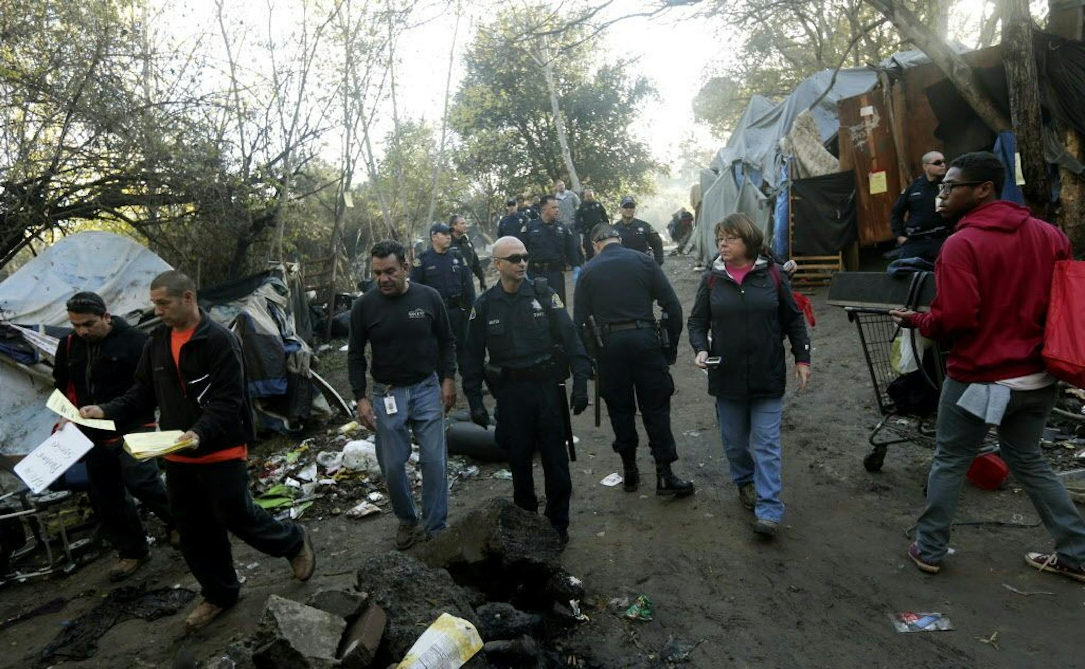 FILE - In this Monday, Dec. 1, 2014, file photo, police officers and city officials hand out warning notices at a Silicon Valley homeless encampment known as The Jungle, in San Jose, Calif.