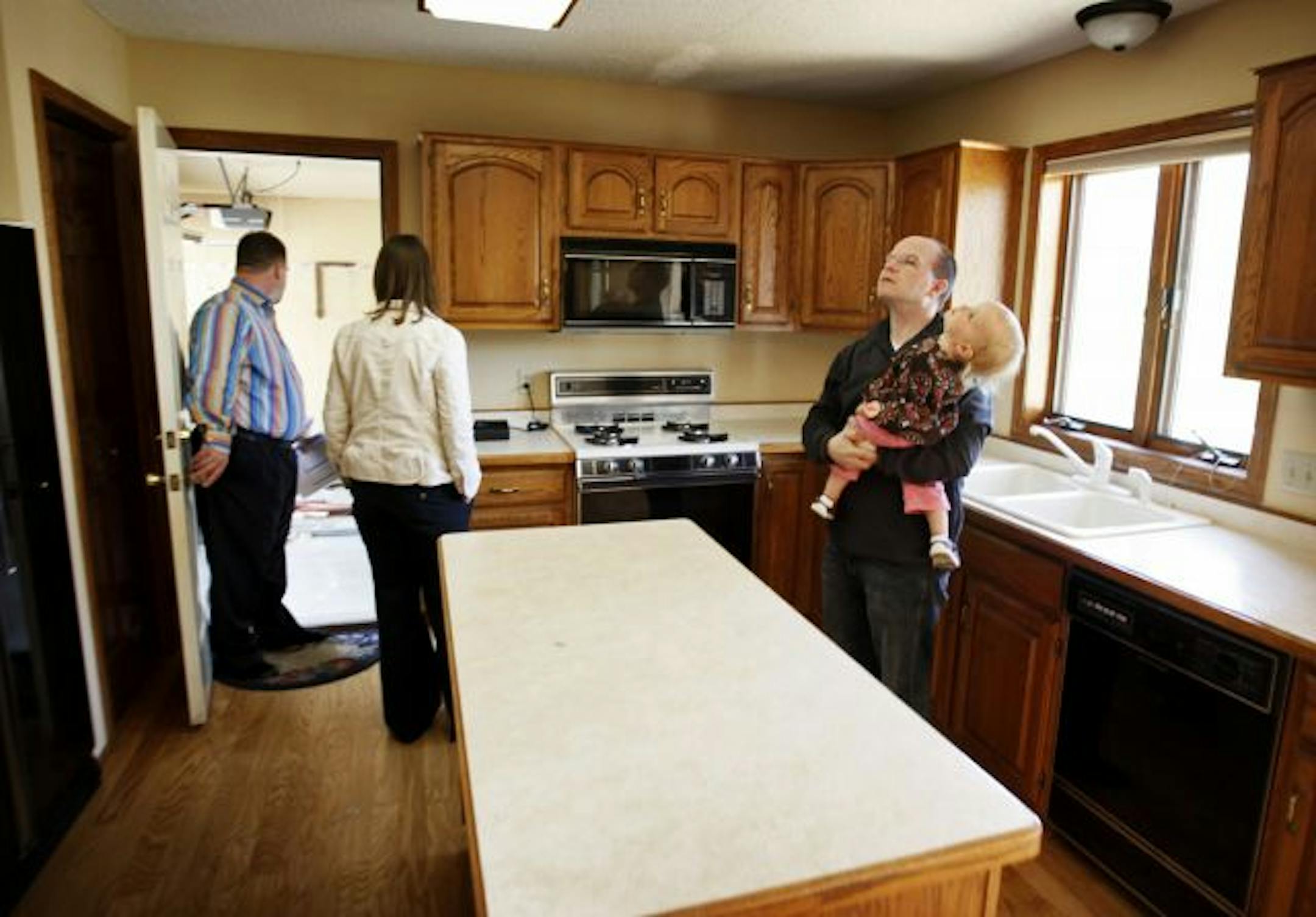 Tony holds daughter Hayden, 19 months, as the pair check out the kitchen ceiling and his wife Bethany, middle, and realtor Jim Starr look out into an attached garage on a foreclosed 4 bedroom, 3,100 square foot home on the market in Eden Prairie.