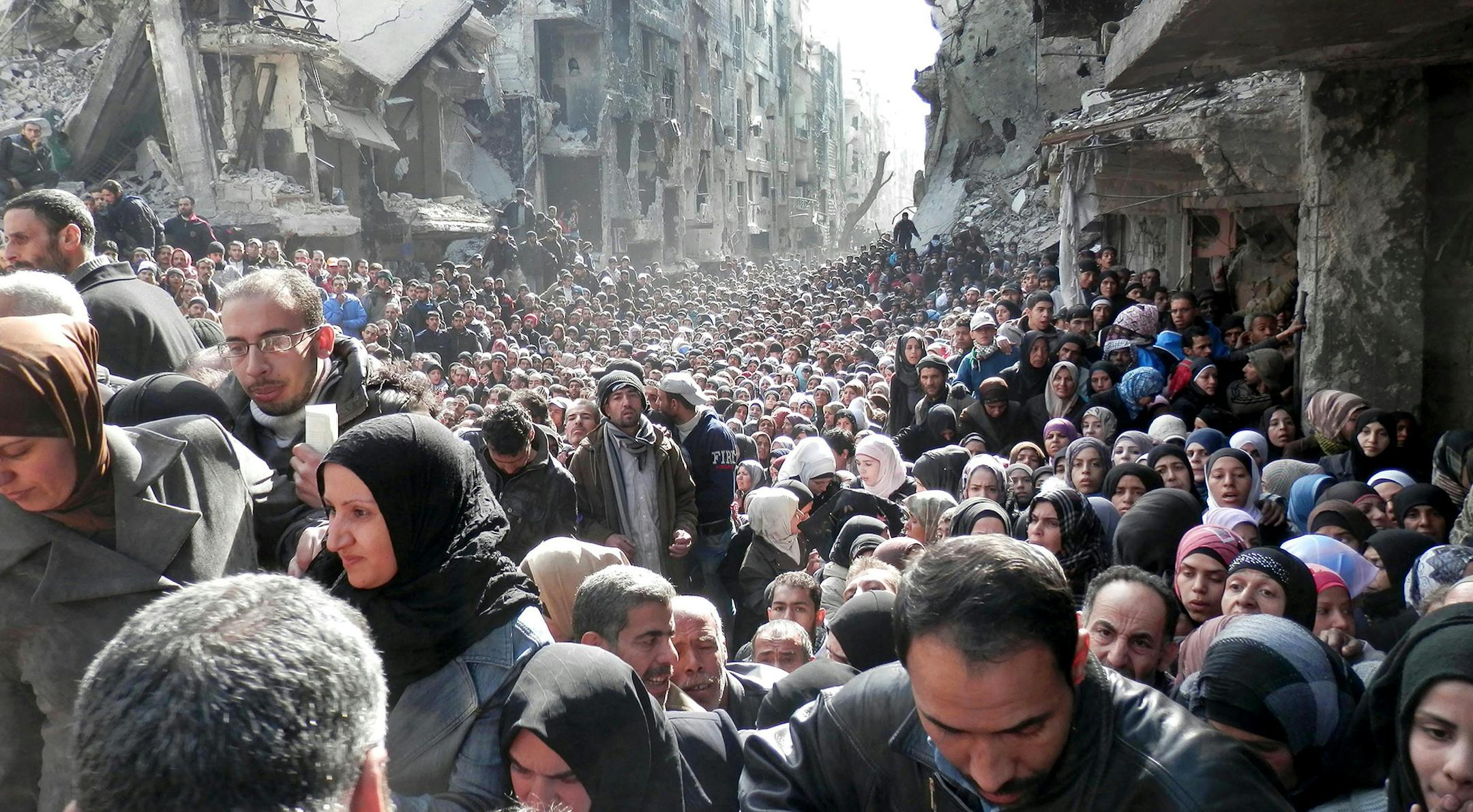 FILE - This picture taken on Jan. 31, 2014, and released by the United Nations Relief and Works Agency for Palestine Refugees (UNRWA), shows residents of the besieged Palestinian camp of Yarmouk, queuing to receive food supplies, in Damascus, Syria. From the three-year-old boy who washed ashore on a Turkish beach to the 71 migrants who suffocated in a truck in Austria to the daily scenes of chaos unfolding in European cities as governments try to halt a human tide heading north. There is no let