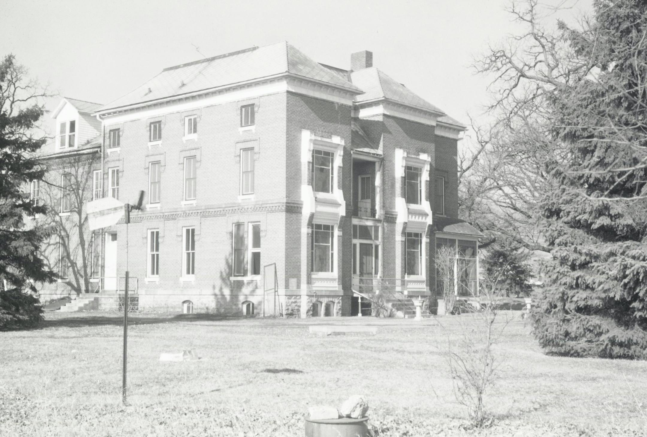 The image shows a large brick building with two full floors, a basement, and an upper floor which is reduced by the roof. Trees frame the building.