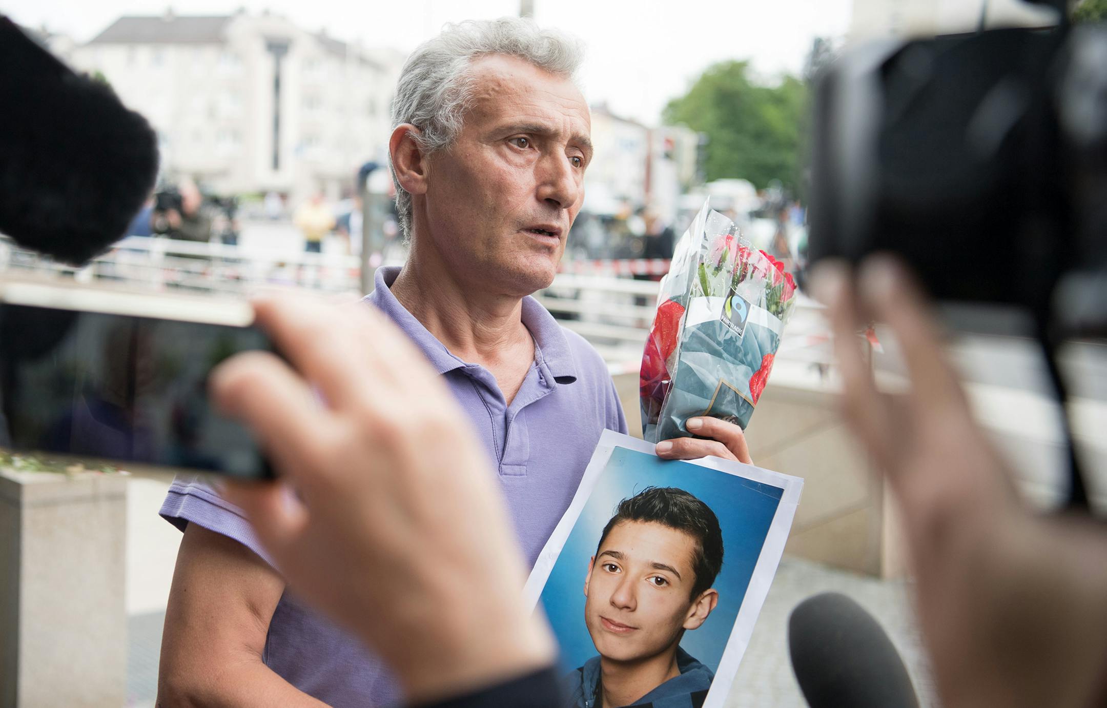 The father of a victim shows a picture of his son near the Olympia shopping center where a shooting took place leaving nine people dead the day before on Saturday, July 23, 2016 in Munich, Germany. (AP Photo/Sebatian Widmann) ORG XMIT: MIN2016072711520163