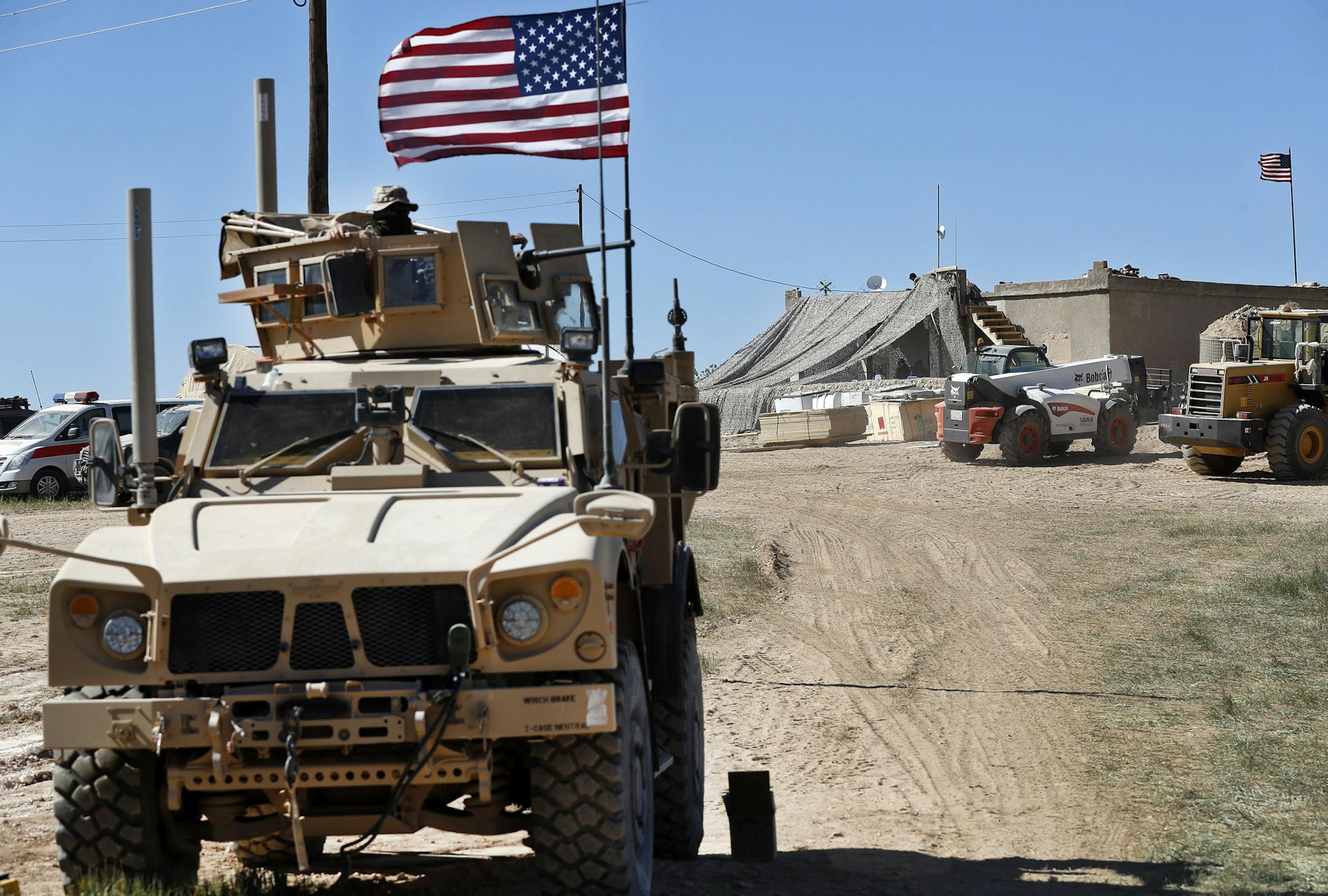 FILE - In this Wednesday, April 4, 2018 file photo, a U.S. soldier, left, sits on an armored vehicle behind a sand barrier at a newly installed position near the front line between the U.S-backed Syrian Manbij Military Council and the Turkish-backed fighters, in Manbij, north Syria. An American military official said Friday, Jan. 11, 2019 that the U.S.-led military coalition has begun the process of withdrawing troops from Syria. (AP Photo/Hussein Malla, File)