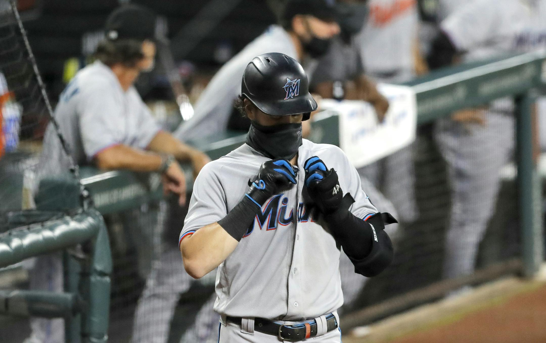Miami Marlins' Brian Anderson wears a face mask to protect against COVID-19 as he buttons his jersey at the on deck circle during the first inning of a baseball game against the Baltimore Orioles, Tuesday, Aug. 4, 2020, in Baltimore. (AP Photo/Julio Cortez)