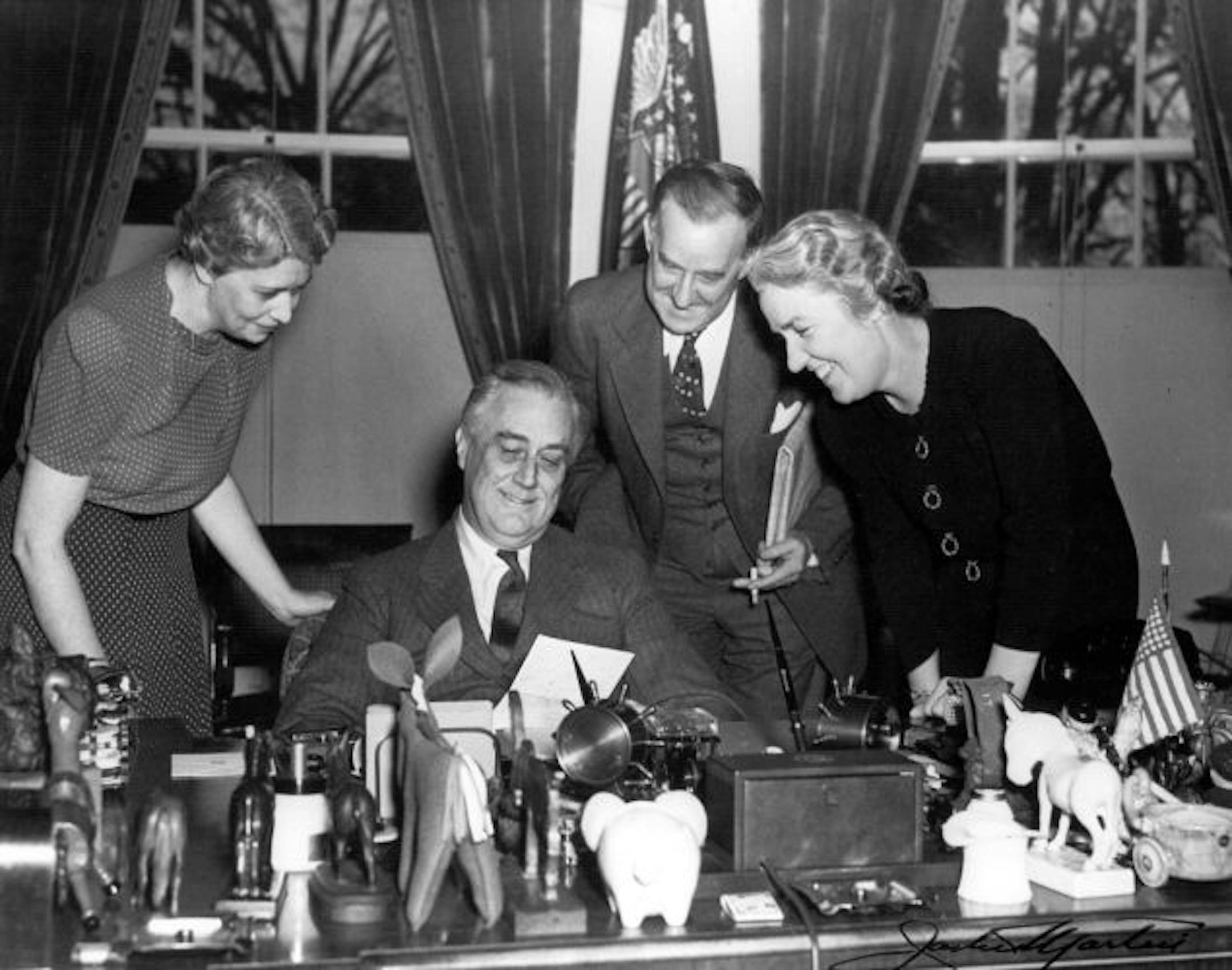 From the library collection, a photo shows President Roosevelt at his desk in the White House with (left to right) Marguerite LeHand, Stephen Early, and Grace Tully, May 22, 1941.