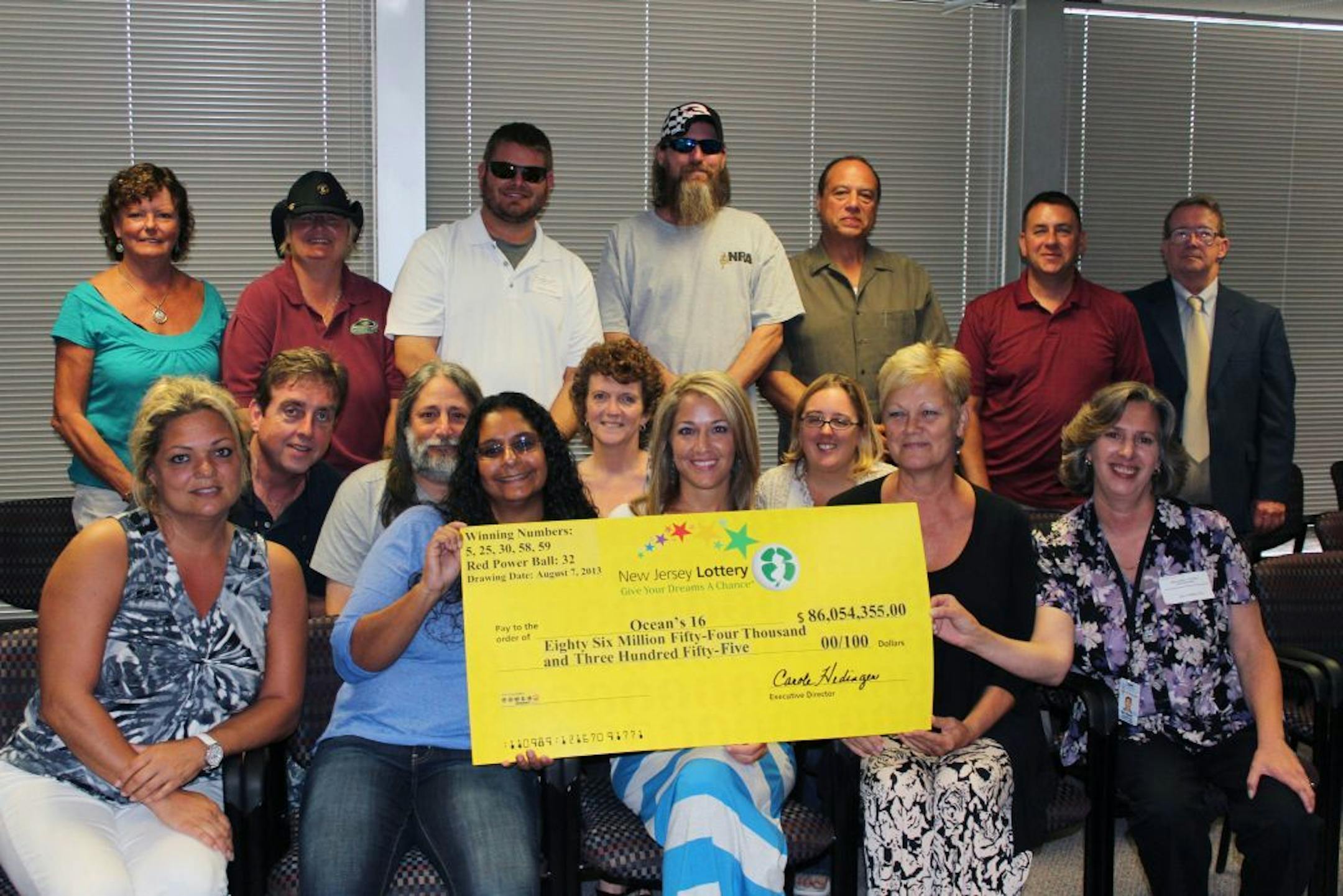 In this Monday, Aug. 12, 2013 photo provided by the New Jersey Lottery, the 16 unidentified workers from an Ocean County garage in a New Jersey shore community hit hard by Superstorm Sandy pose with a winner's check from the $448 million Powerball drawing, on Wednesday, Aug. 7. The group had one of three winning tickets in the lottery.
