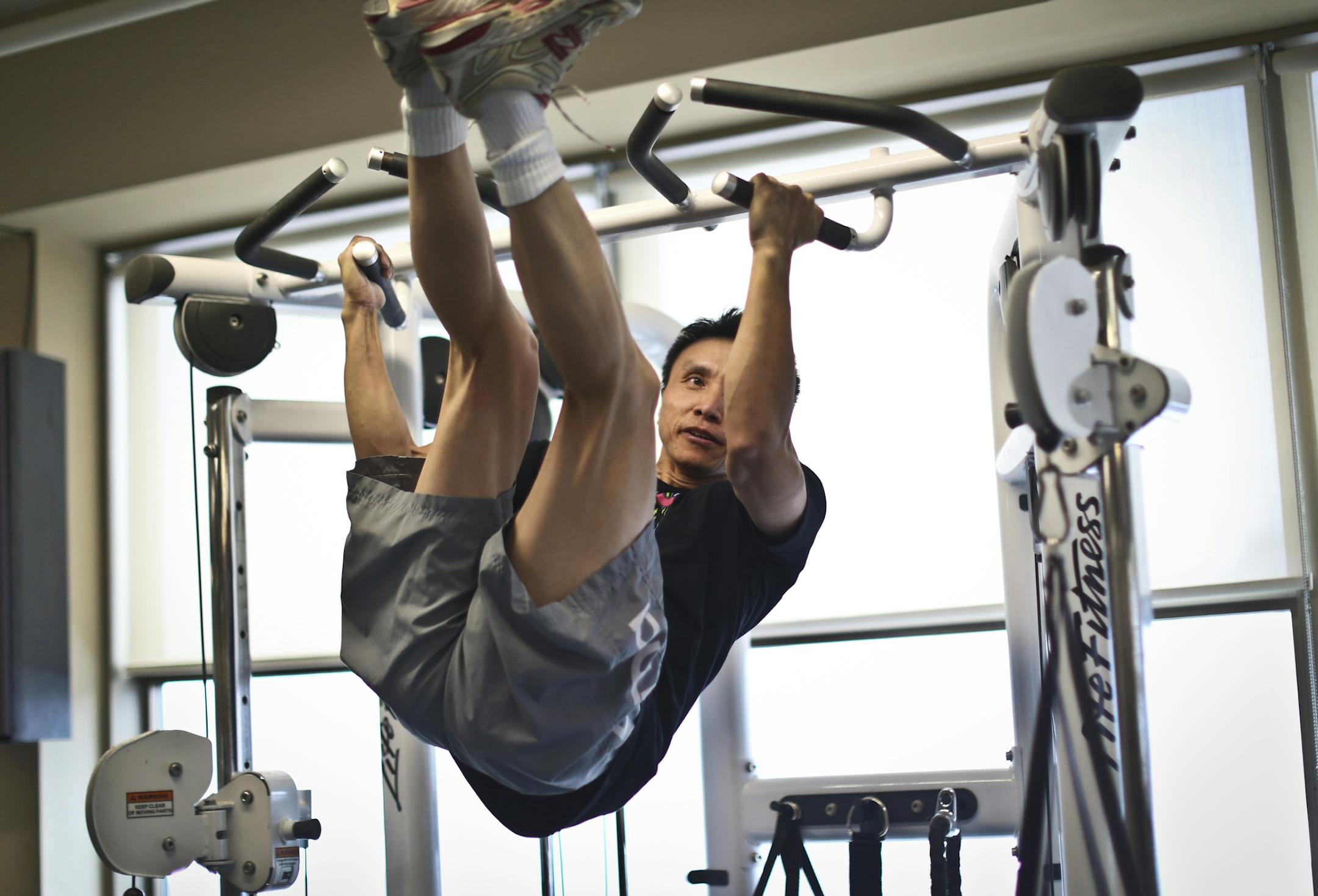 St. Paul police officer Loue Vang did what he called a windshield wiper exercise (where he waved his legs back and forth in a pull-up position) at the department gym on Friday, March 15, 2013, in St. Paul, Minn. ] (RENEE JONES SCHNEIDER * reneejones@startribune.com)
