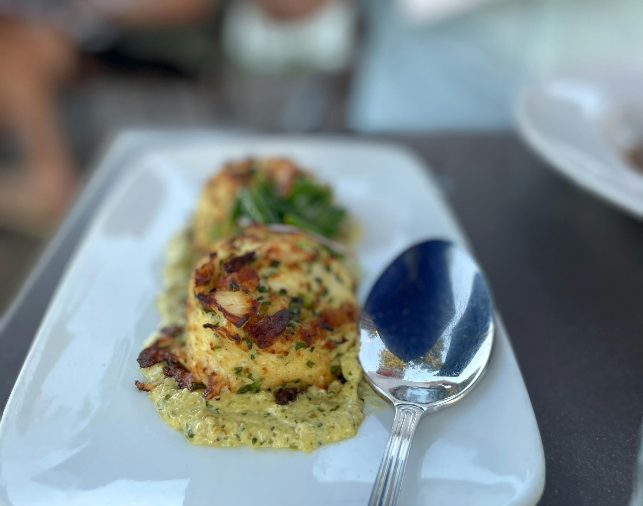 Two giant crab cakes on a sauce on a white plate.