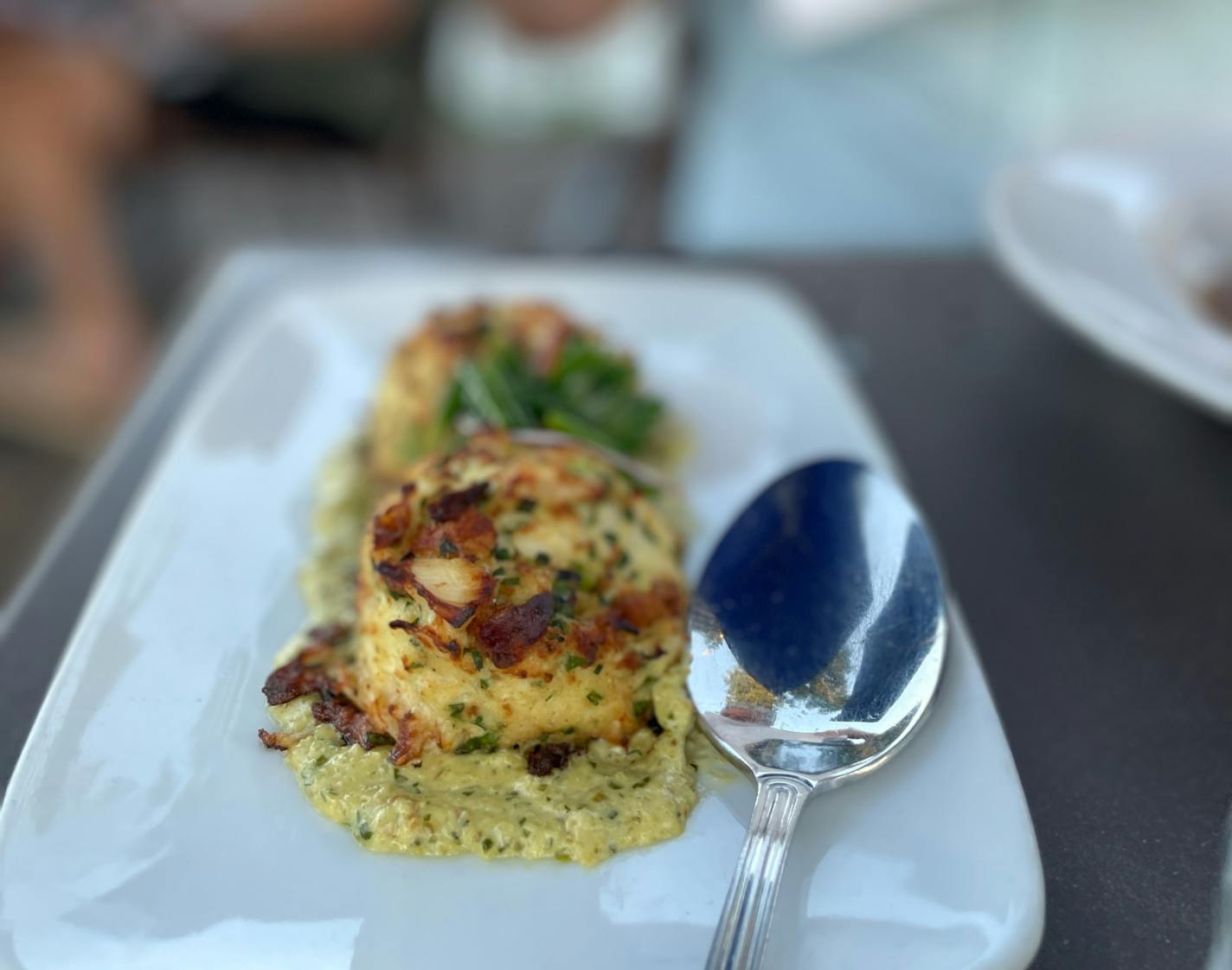 Two giant crab cakes on a sauce on a white plate.