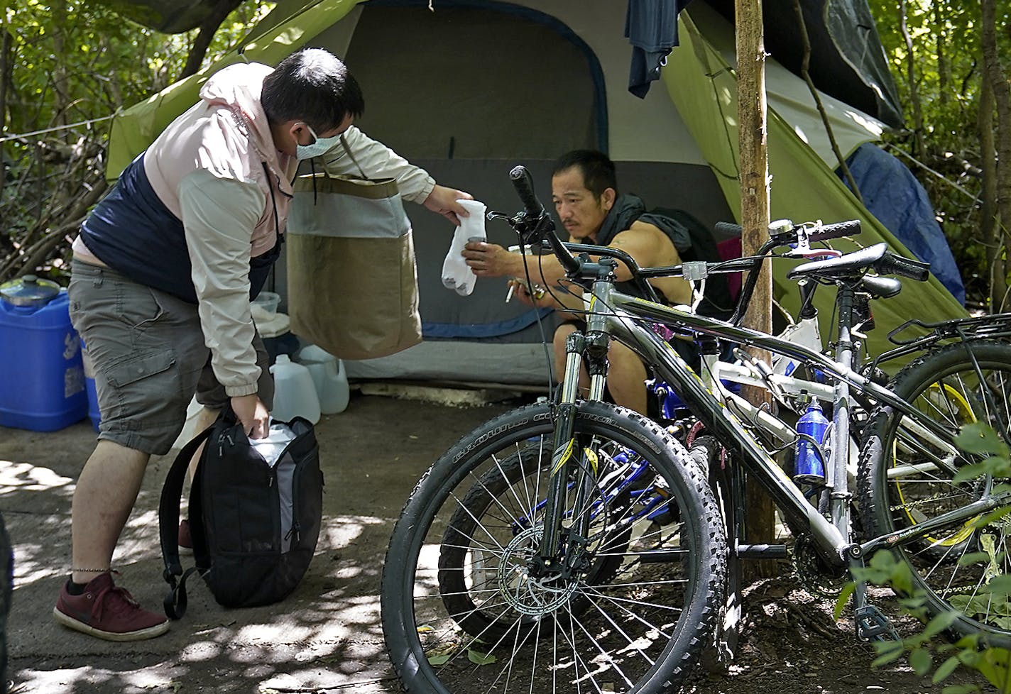 Tony Vang, a street outreach case manager for People Incorporated, right, brought a sleeping bag, food, water and new socks to a small homeless encampment of Hmong residents Thursday in a wooded area in east St. Paul. Here, Vang, left, handed new socks to encampment resident Tou Vang, 41.] DAVID JOLES • david.joles@startribune.com Thousands of Minnesotans who are poor, elderly or have disabilities will get more help staying in their own homes and avoid becoming homeless under an innovative Medic