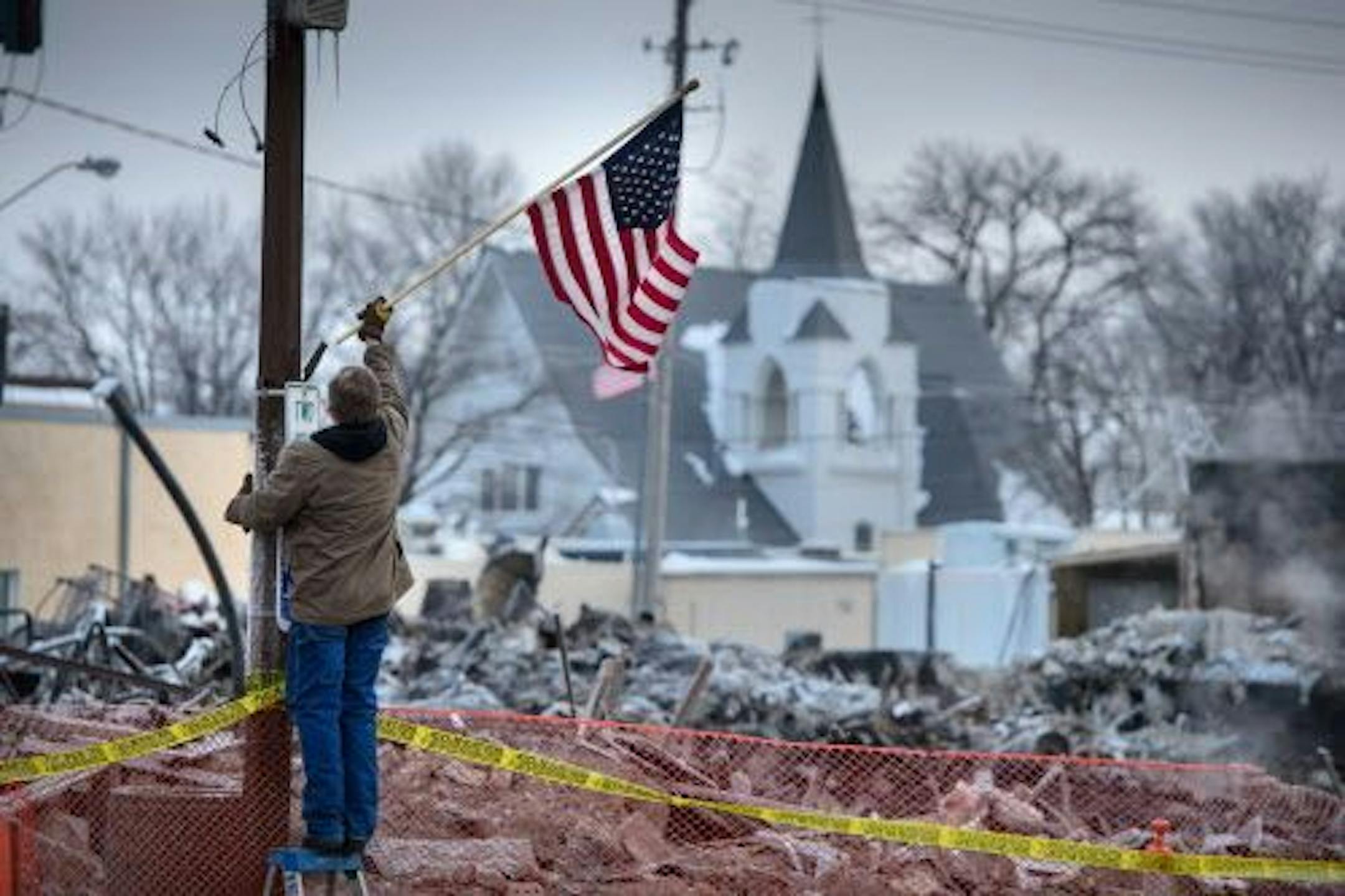 Madelia street supervisor Mark Blekestad placed American flags along Main Street, where a fire this week destroyed six buildings on a downtown block.