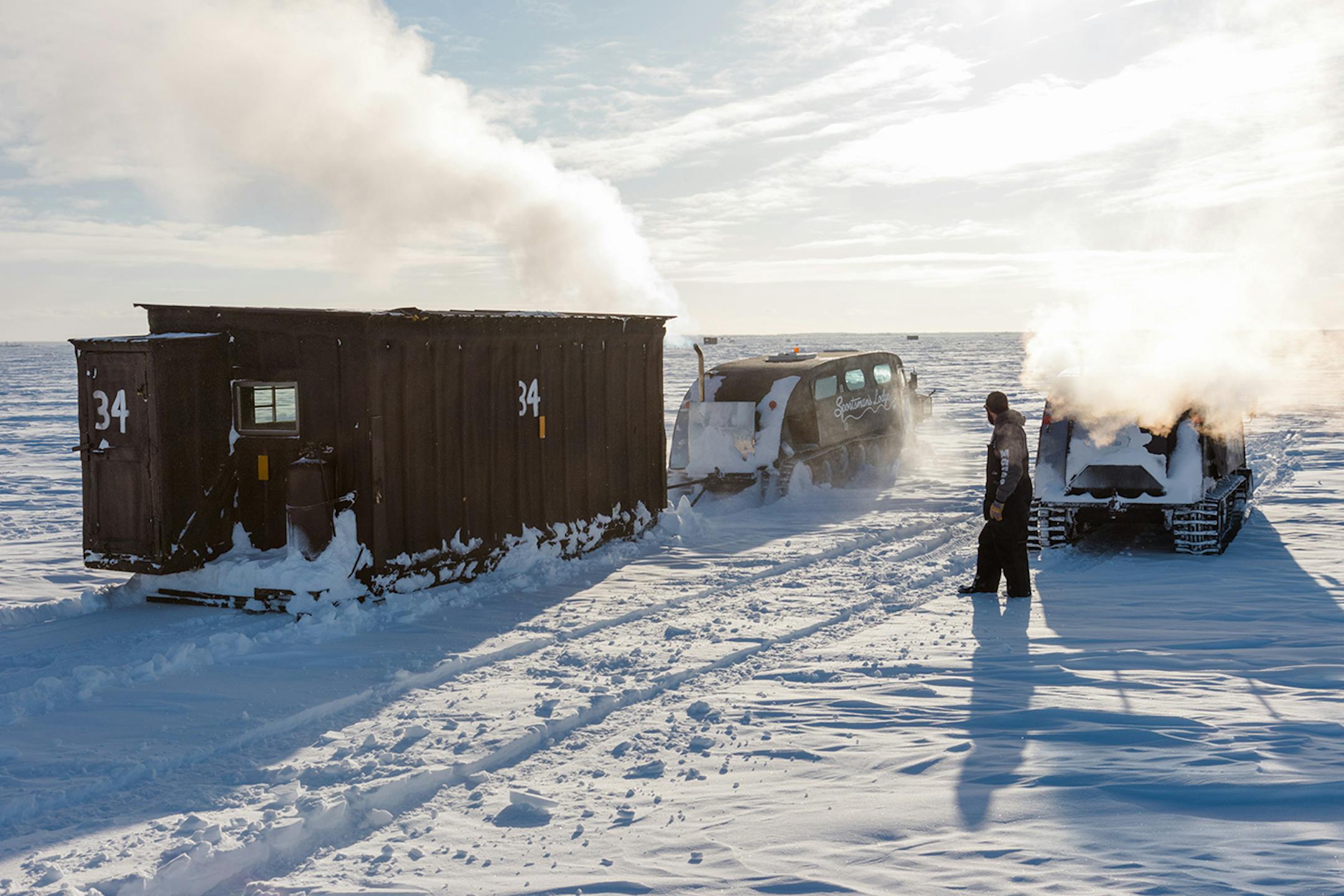 Luke Eiynck stands by as a bombardier drags an ice house through the snow. The guides work together to move ice houses quickly.
