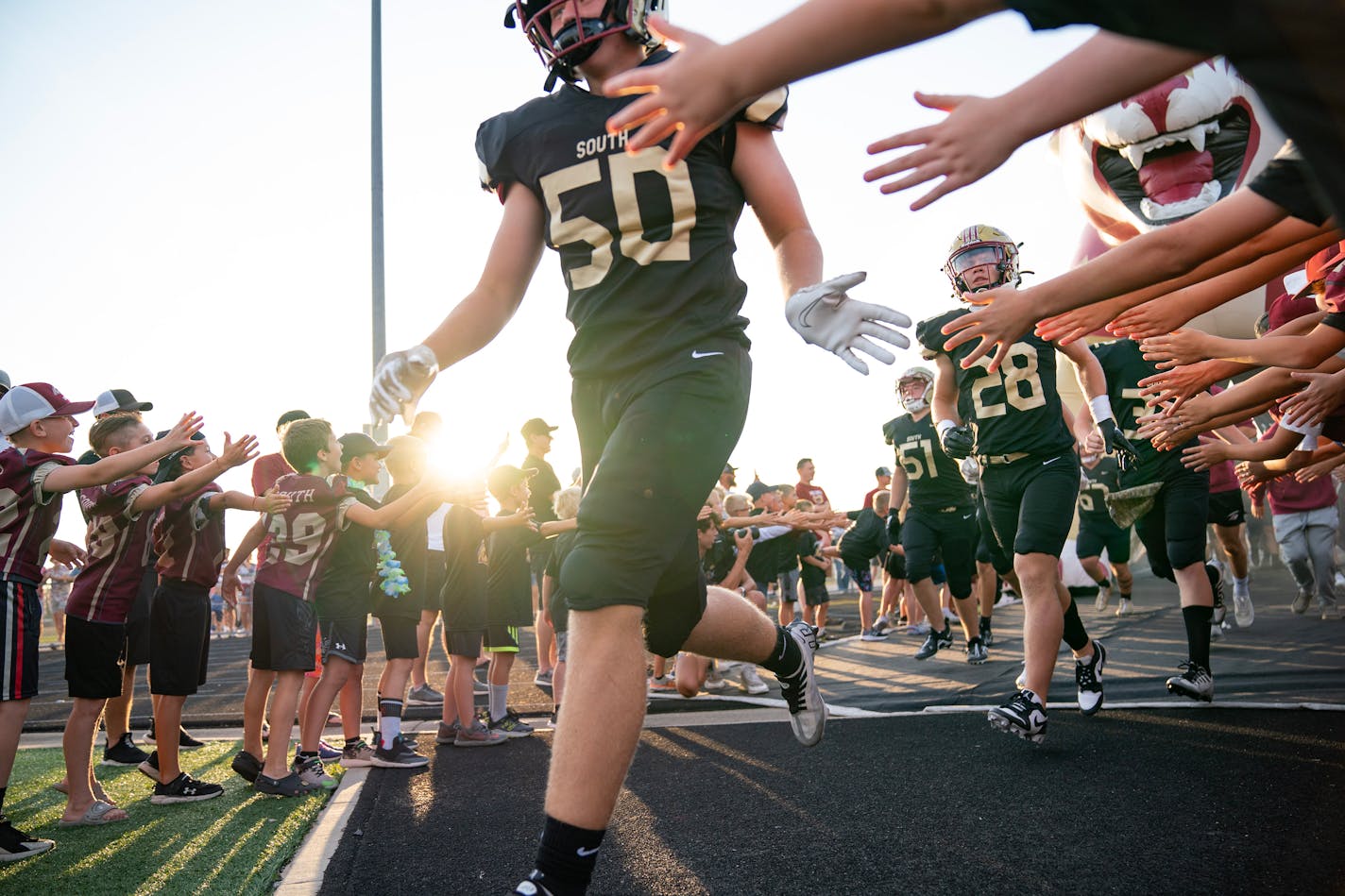 Lakeville South players run out of the tunnel between lines of youth football players before their season opener against Wayzata Friday, Sep. 01, 2023, at Lakeville South High School in Lakeville, Minn. ]