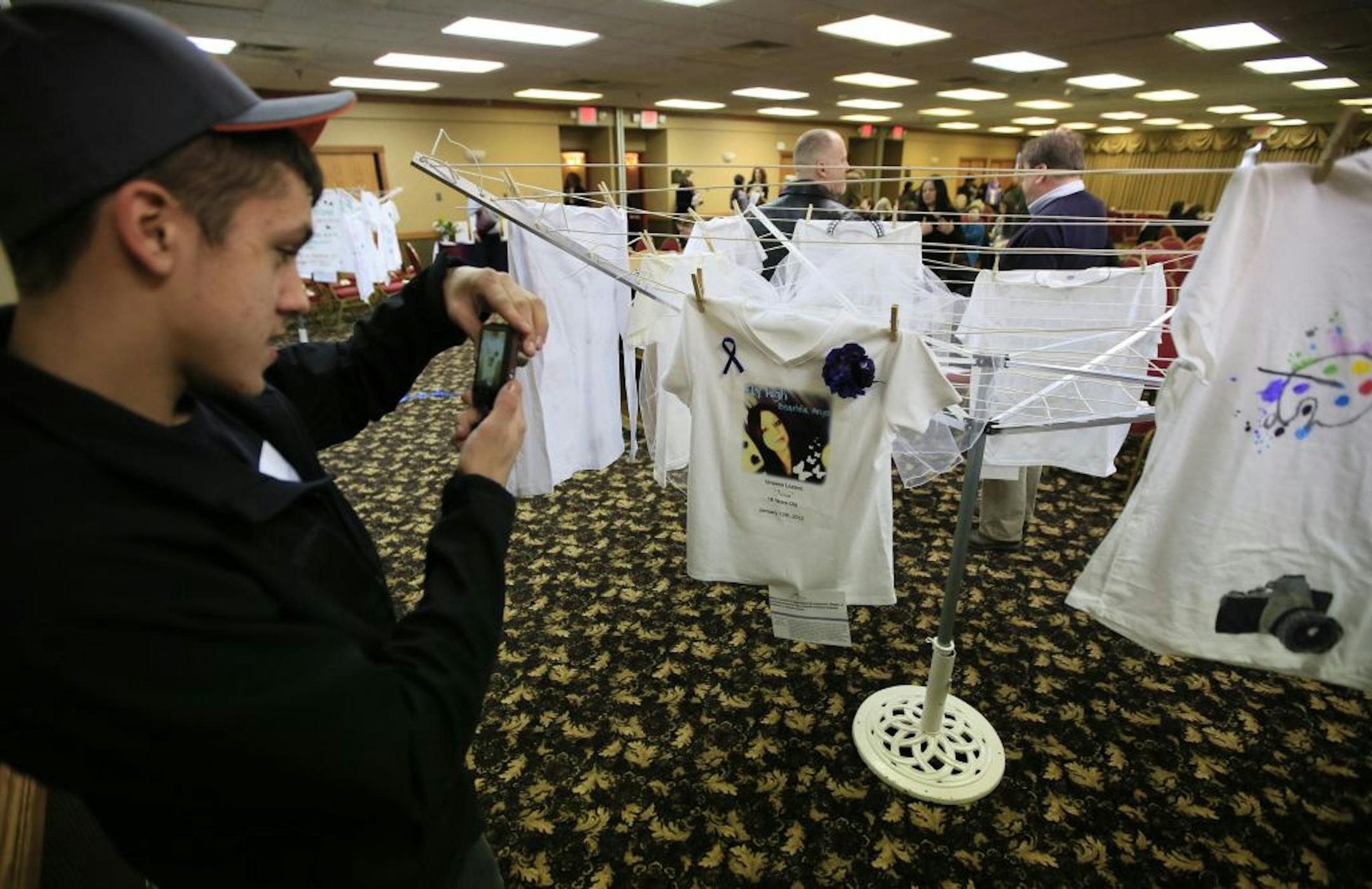 Emmitt Lozano, 15, take a picture of his sisters memorial shirt that hangs on the Clothsline Project memorial during a Domestic Violence Homicide Memorial Reception Thuesday afternoon at the Kelly Inn in St. Paul. Lozano's sister Vinessa was killed by a coworker January 13th 2012, when she turned away his advances.