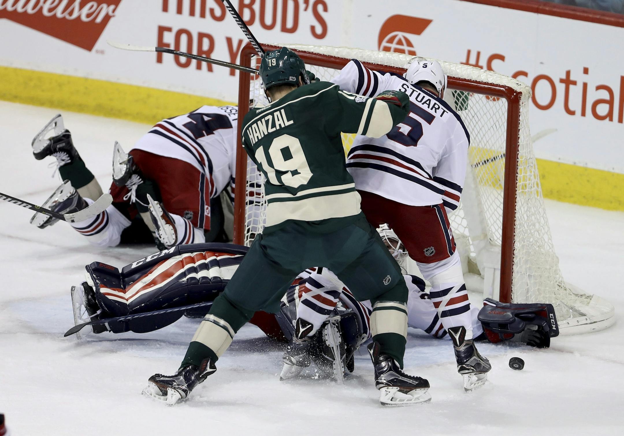 Winnipeg Jets goaltender Michael Hutchinson (34) stretches out and makes a save with Jets' Mark Stuart (5) battling Minnesota Wild's Martin Hanzal (19) in front of the net during the third period of an NHL hockey game in Winnipeg, Manitoba, Sunday, March 19, 2017.