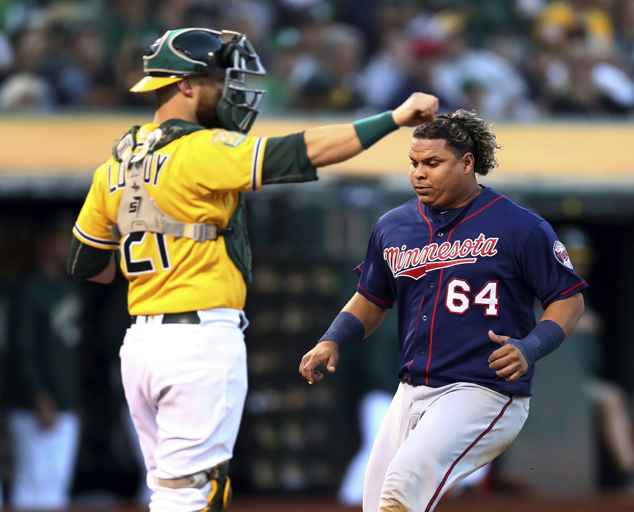 Minnesota Twins' Willians Astudillo, right, scores past Oakland Athletics catcher Jonathan Lucroy (21) in the third inning of a baseball game Saturday, Sept. 22, 2018, in Oakland, Calif. Astudillo scored on a sacrifice fly by the Twins' Joe Mauer. (AP Photo/Ben Margot)