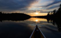 The sun set in front of the bow of a Wenonah Minnesota II canoe in The Boundary Waters Canoe Area Wilderness on Eddy Lake in the Fall Lake Township. ]