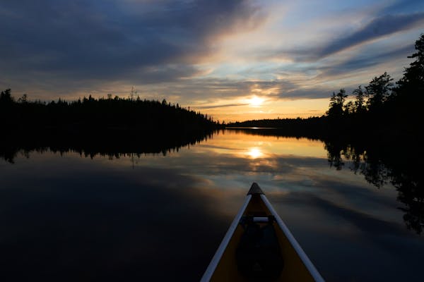 The sun set in front of the bow of a Wenonah Minnesota II canoe in The Boundary Waters Canoe Area Wilderness on Eddy Lake in the Fall Lake Township. ]