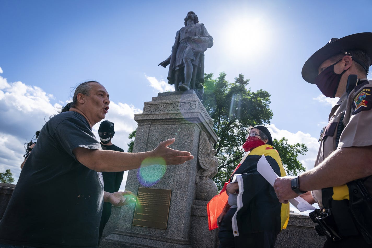 Mike Forcia, left, talks with a Minnesota State Trooper about safely taking down the statue of Christopher Columbus, background, with no arrests before activists pulled down the statue, in front of the Minnesota State Capitol, Wednesday, June 10, 2020, in St. Paul, Minn. (Leila Navidi/Star Tribune via AP)