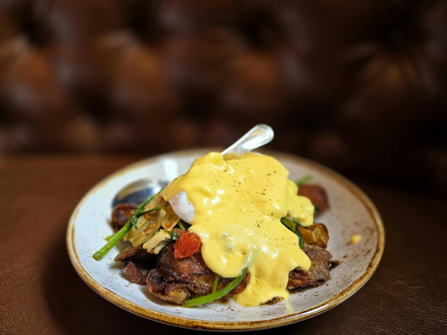 A bowl with brown crispy potatoes and other colorful vegetables, topped with a yellow hollandaise sauce