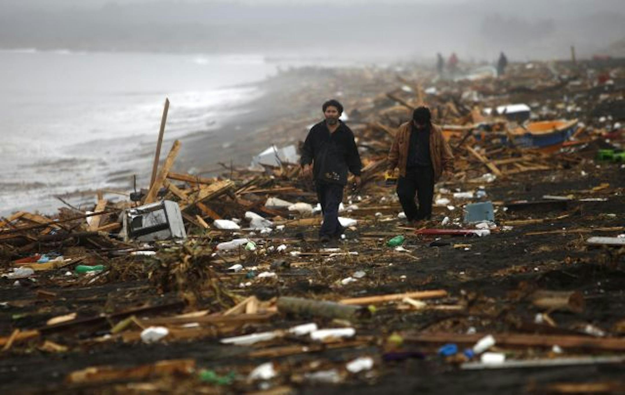 People walked Sunday along the shore of Pelluhue, where strong waves triggered by Saturday's quake obliterated homes, and boats were found on land, next to overturned cars.
